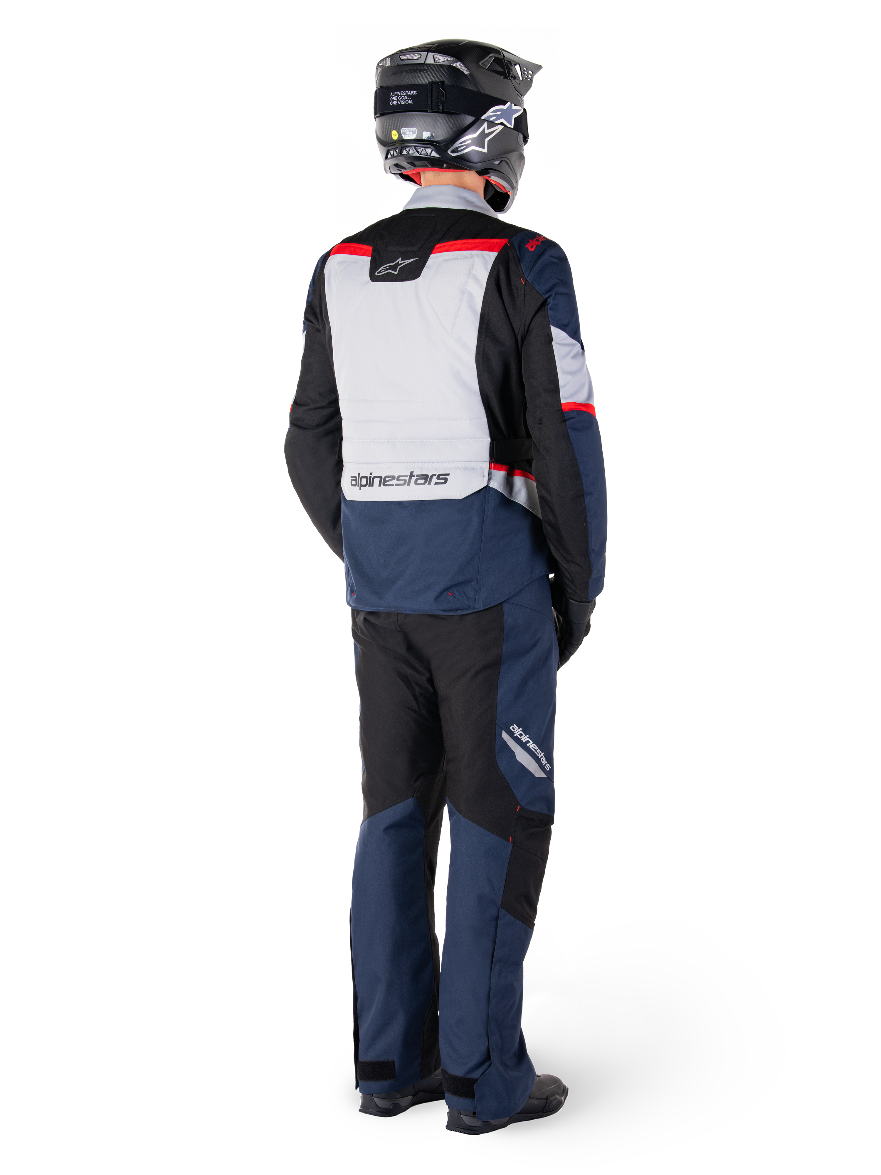 Achteraanzicht van een motorrijder in Alpinestars ST-1 Waterproof broek en bijpassend jack in Dark Blue Black en Bright Red, adventure touring-uitrusting met textielpanelen en reflecterende accenten, gecombineerd met een zwarte helm en laarzen