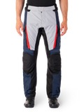 Alpinestars ST-1 waterdichte broek, motortoerbroek, donkerblauw en lichtgrijs met felrode accenten, zwarte versterkte kniepanelen, vooraanzicht gedragen met zwarte laarzen, waterdichte adventure touring uitrusting