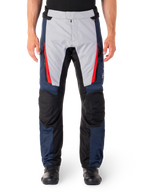 Alpinestars ST-1 waterdichte broek, motortoerbroek, donkerblauw en lichtgrijs met felrode accenten, zwarte versterkte kniepanelen, vooraanzicht gedragen met zwarte laarzen, waterdichte adventure touring uitrusting