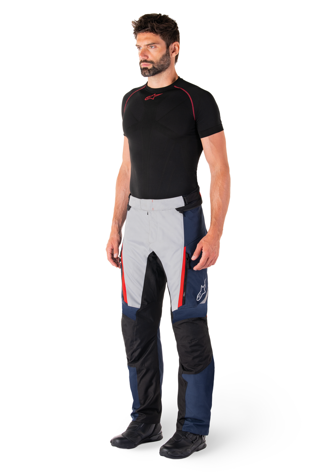 Alpinestars St-1 Waterproof broek, motor tourbroek, donkerblauw, zwart en helderrood, gedragen door model met zwarte basislaag en zwarte laarzen, voorzien van zakken met ritssluiting en Alpinestars-logo op de broekspijp