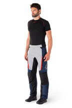 Alpinestars St-1 Waterproof broek, motor tourbroek, donkerblauw, zwart en helderrood, gedragen door model met zwarte basislaag en zwarte laarzen, voorzien van zakken met ritssluiting en Alpinestars-logo op de broekspijp