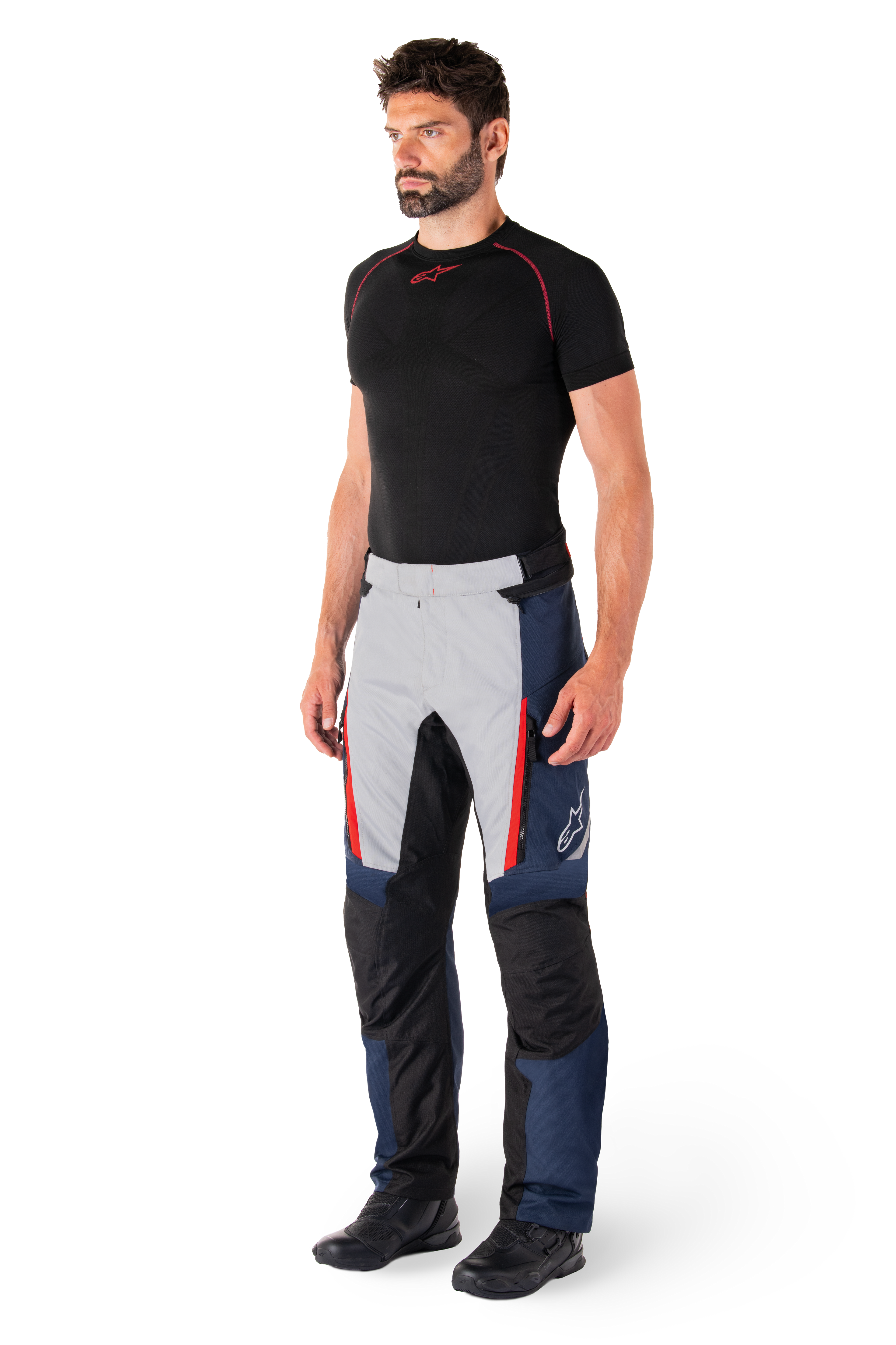Alpinestars St-1 Waterproof broek, motor tourbroek, donkerblauw, zwart en helderrood, gedragen door model met zwarte basislaag en zwarte laarzen, voorzien van zakken met ritssluiting en Alpinestars-logo op de broekspijp