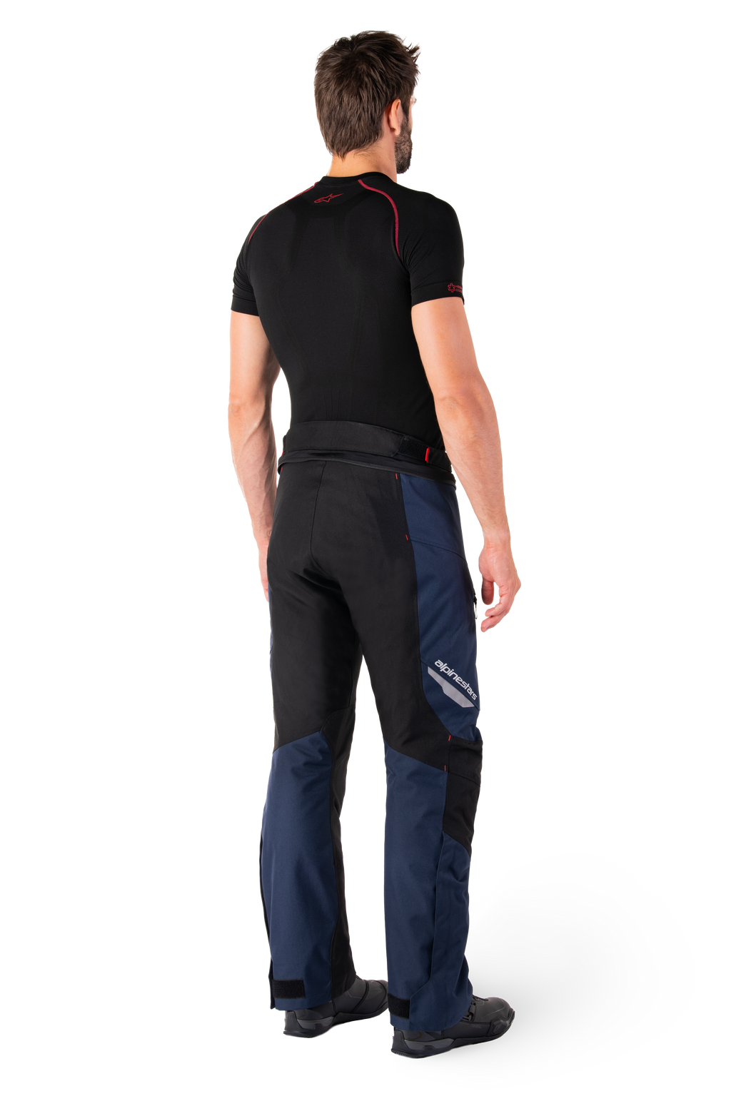 Alpinestars St-1 Waterproof broek, adventure touring broek, donkerblauw, zwart en felrood, achteraanzicht van de zijkant, gedragen met een zwarte basislaag met korte mouwen en zwarte motorlaarzen, gestroomlijnd ontwerp met reflecterende branding en rode accenten