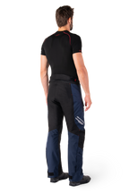 Alpinestars St-1 Waterproof broek, adventure touring broek, donkerblauw, zwart en felrood, achteraanzicht van de zijkant, gedragen met een zwarte basislaag met korte mouwen en zwarte motorlaarzen, gestroomlijnd ontwerp met reflecterende branding en rode accenten