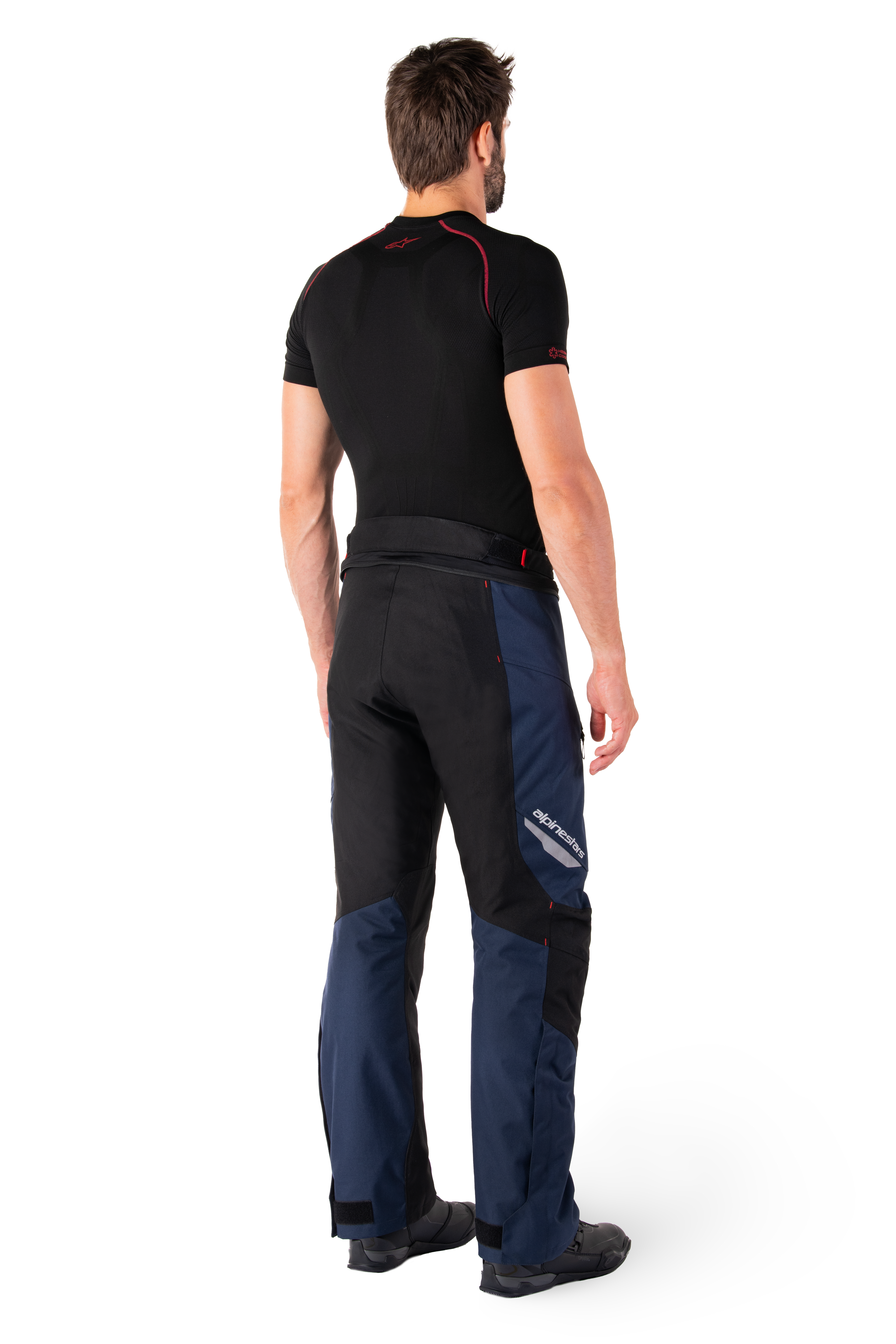 Alpinestars St-1 Waterproof broek, adventure touring broek, donkerblauw, zwart en felrood, achteraanzicht van de zijkant, gedragen met een zwarte basislaag met korte mouwen en zwarte motorlaarzen, gestroomlijnd ontwerp met reflecterende branding en rode accenten