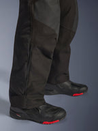 Alpinestars Andes V4 Drystar® Broek - Lang, zwarte adventure motorbroek, close-up van het onderbeen met verstelbare ritssluiting bij de enkel en duurzame textielconstructie, gedragen met zwarte motorlaarzen met rode accenten