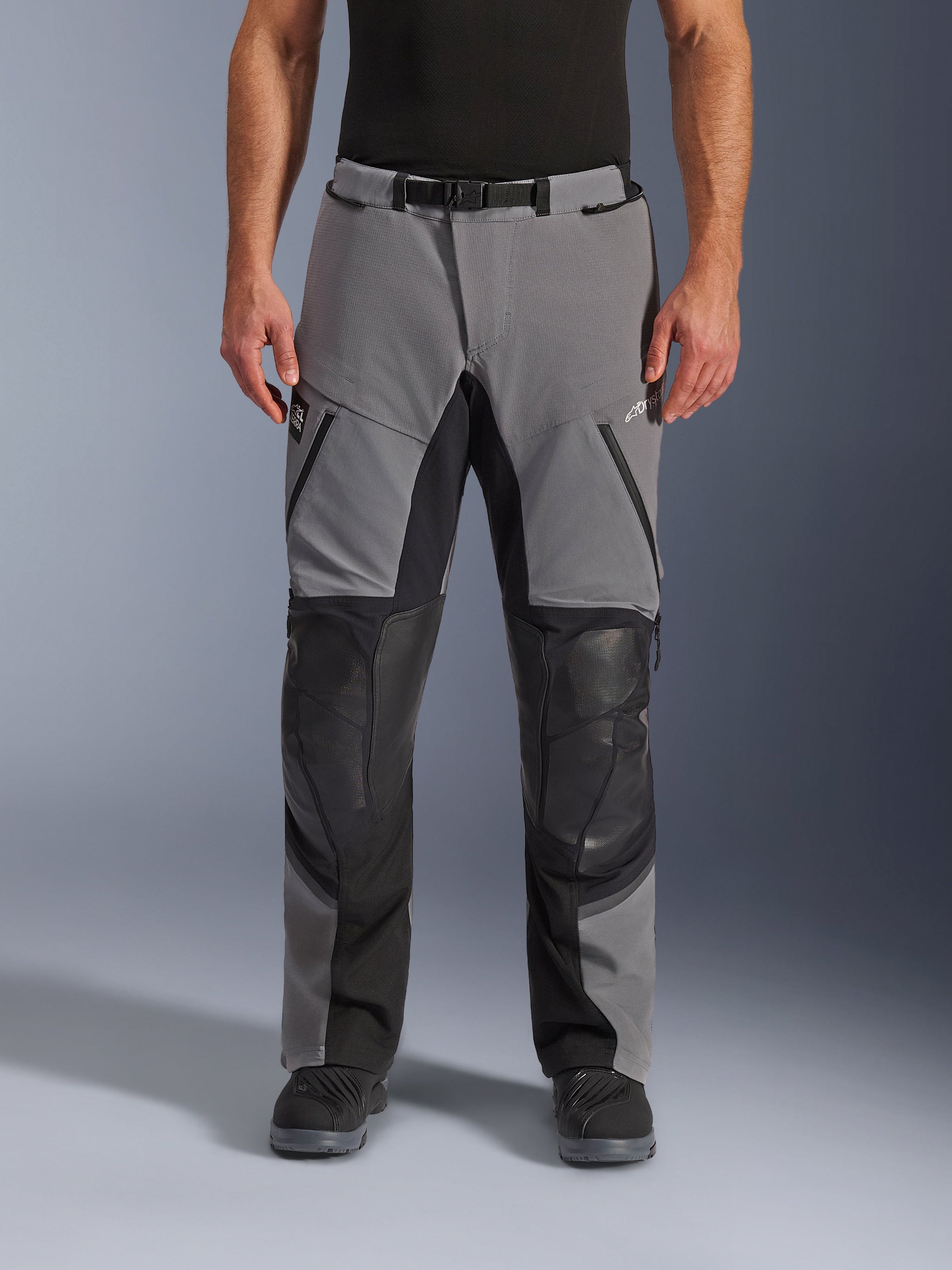 Alpinestars Andes Pro Drystar® XF broek, motorbroek, donkergrijs en zwart, vooraanzicht, voorzien van versterkte zwarte kniepanelen, waterdichte ritsen en een riem met magnetische gesp, gedragen met zwarte laarzen