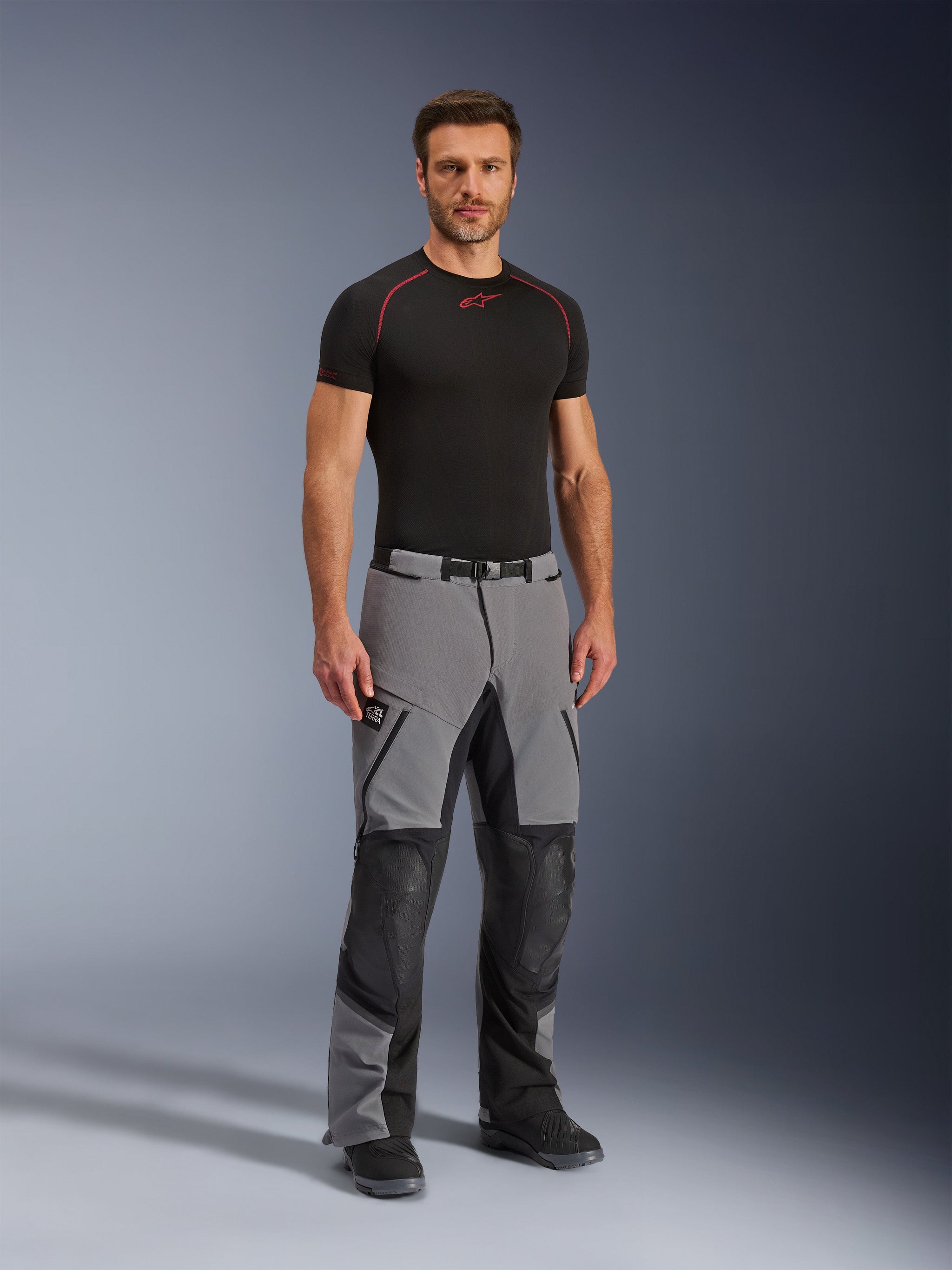 Alpinestars Andes Pro Drystar® XF broek, adventure motorbroek, donkergrijs en zwart, gedragen door een model met een zwarte technische basislaag, voorzien van een multi-paneel constructie met waterdichte ritsen en versterkte zones voor adventure ritten.