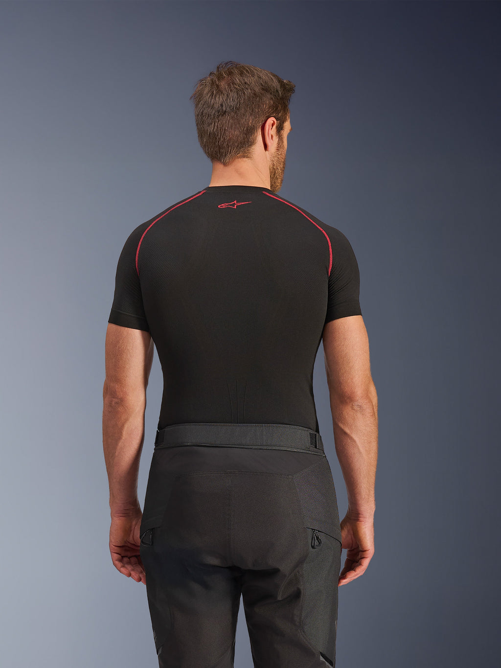 Alpinestars Cusco Drystar® broek, zwarte motorbroek, achteraanzicht van rijder in adventure touring uitrusting met een zwart compressieshirt met korte mouwen en rode stiksels, duurzame ripstop en 600D stofconstructie