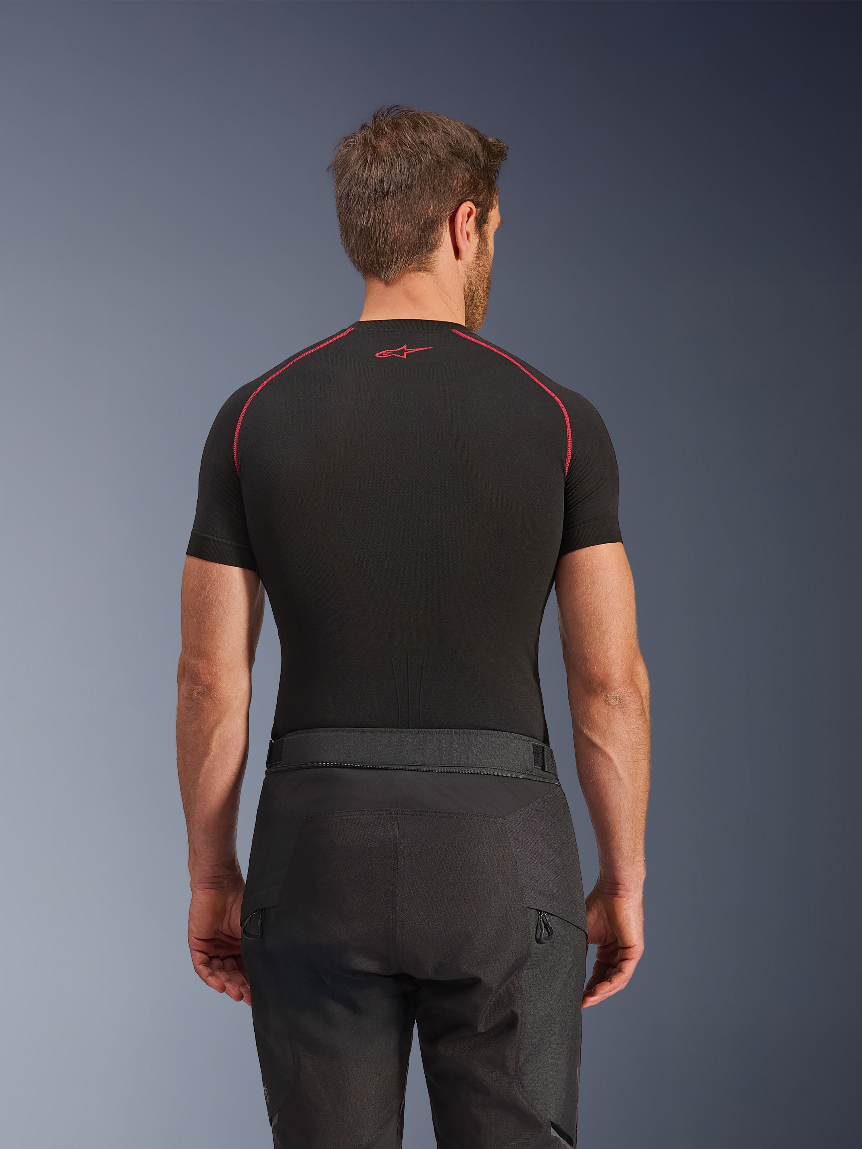 Alpinestars Cusco Drystar® broek, zwarte motorbroek, achteraanzicht van rijder in adventure touring uitrusting met een zwart compressieshirt met korte mouwen en rode stiksels, duurzame ripstop en 600D stofconstructie