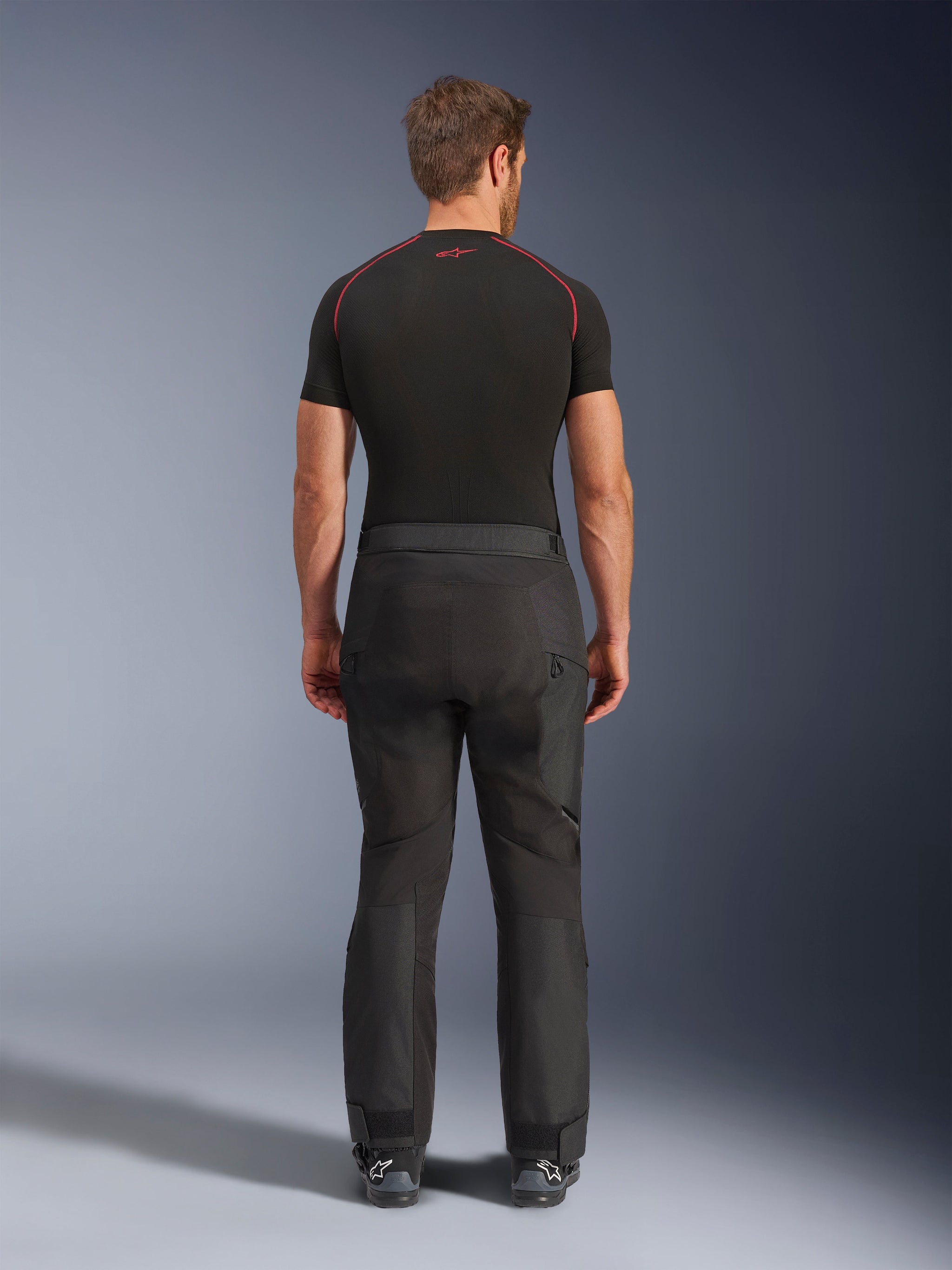 Rijder draagt Alpinestars Cusco Drystar® broek, zwarte adventure motorbroek, achteraanzicht, gecombineerd met een zwart compressieshirt met korte mouwen en zwarte motorlaarzen, voorzien van een duurzaam textielontwerp met voorgevormde panelen voor touring