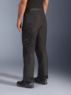 Alpinestars Cusco Drystar® broek, motorbroek, zwart, driekwart achteraanzicht met dijbeenzak met ritssluiting en voorgevormde panelen, gedragen met zwarte motorlaarzen, duurzaam adventure touring-ontwerp met subtiele branding