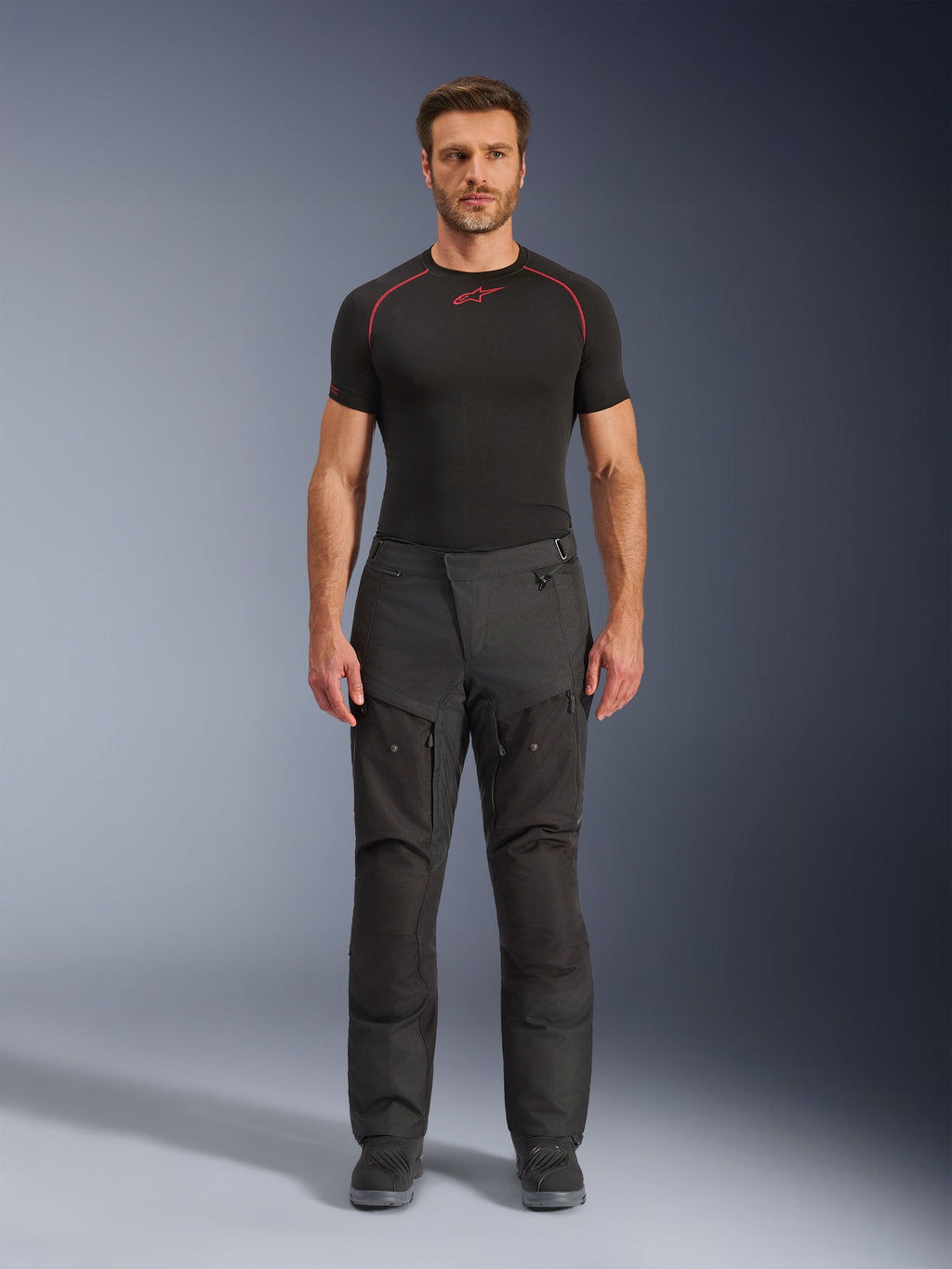 Alpinestars Cusco Drystar® broek, textiel motorbroek, zwart, gedragen door een model met een zwarte basislaag en laarzen, adventure touring-ontwerp met ritsbare ventilatiepanelen op de dijen en duurzame multi-panel constructie