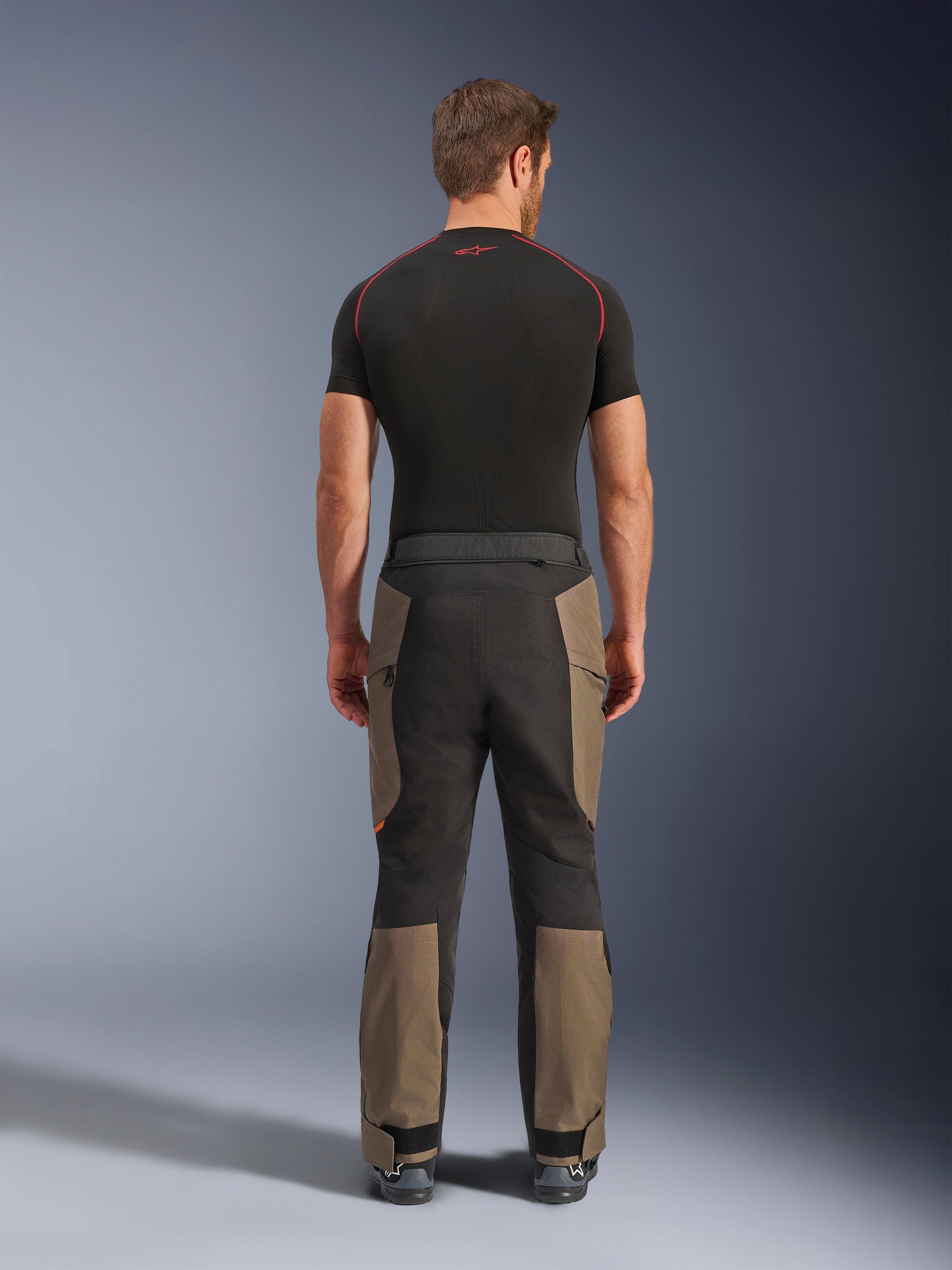 Alpinestars Cusco Drystar® broek, adventure motorbroek, Walnut Black, achteraanzicht met bruine en zwarte panelen, duurzame ripstop-constructie, gedragen met een zwart basislaagshirt