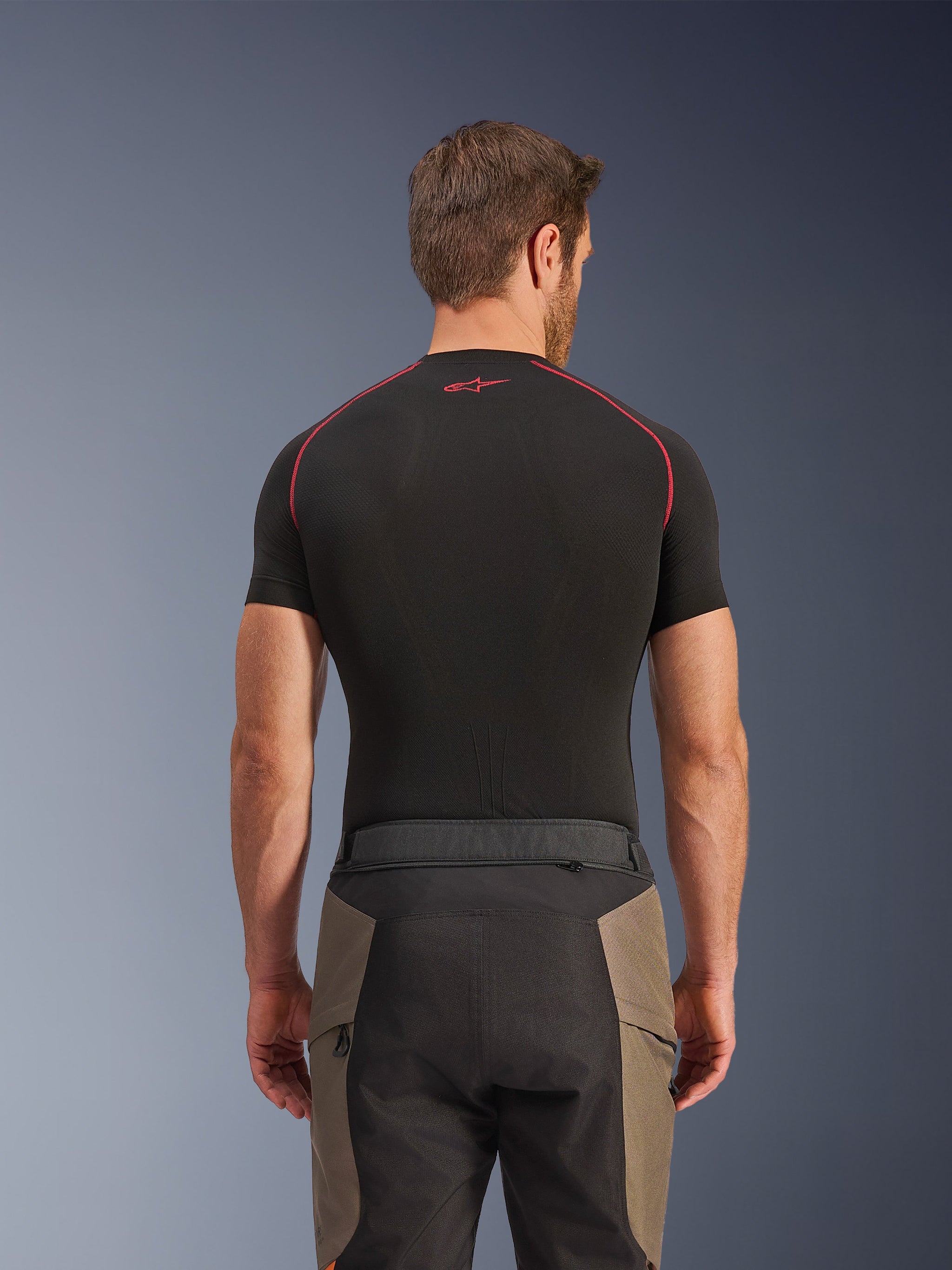 Alpinestars Cusco Drystar® broek, adventure motorbroek, Walnut Black, achteraanzicht met taille-details en een design met kleurvlakken, gedragen met een zwarte basislaag met korte mouwen, rode stiksels en logo