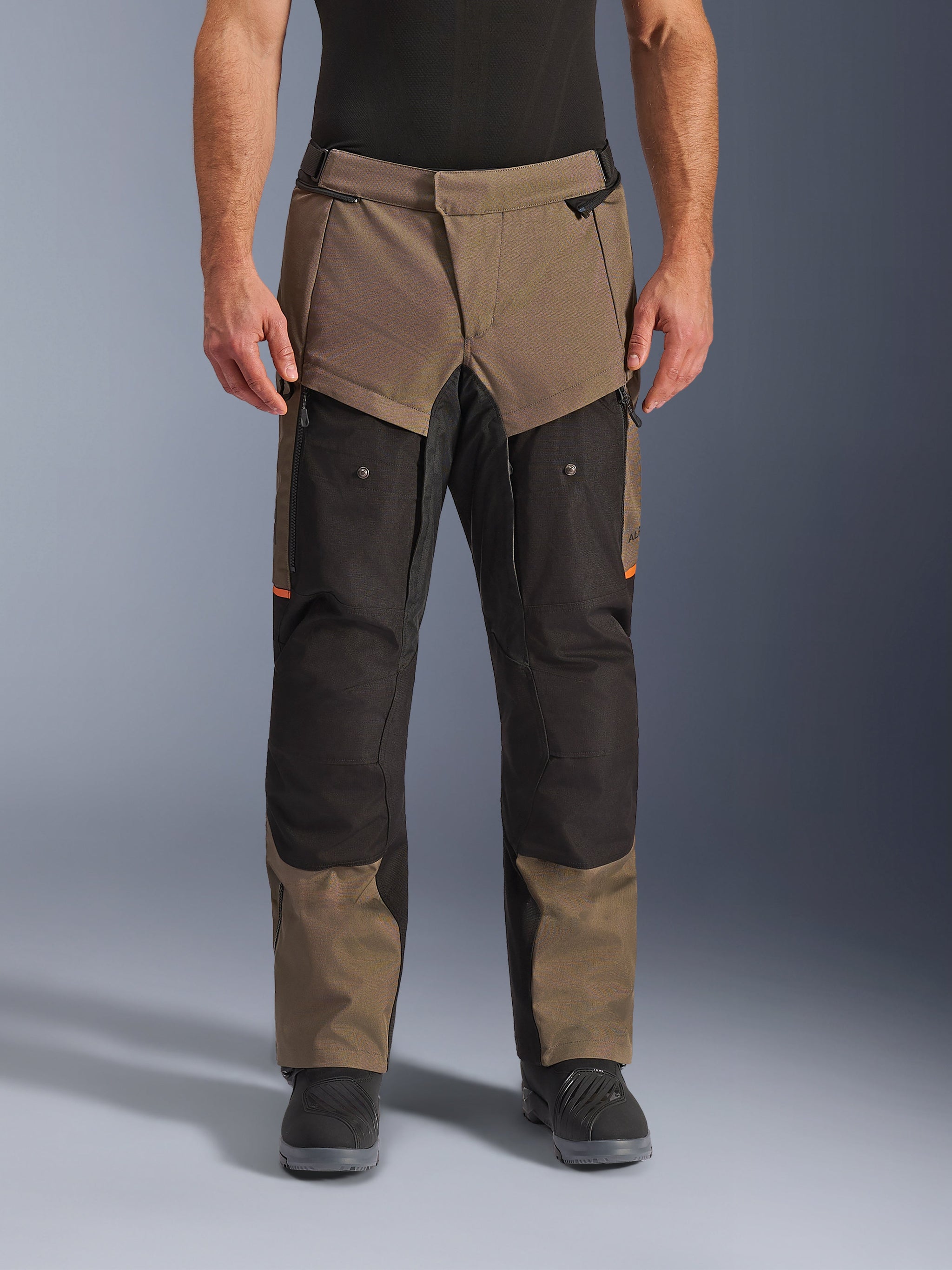 Alpinestars Cusco Drystar® broek, adventure touring motorbroek, walnut en zwart met oranje accenten, vooraanzicht op model, voorzien van technische textielconstructie, cargozakken en ventilatieritsen, gedragen met zwarte motorlaarzen