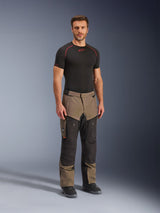 Alpinestars Cusco Drystar® broek, adventure motorbroek, Walnut en zwart, gedragen door een model met een zwarte basislaag en laarzen, met grote cargozakken op de bovenbenen, ventilatieritsen en een robuust tweekleurig ontwerp.