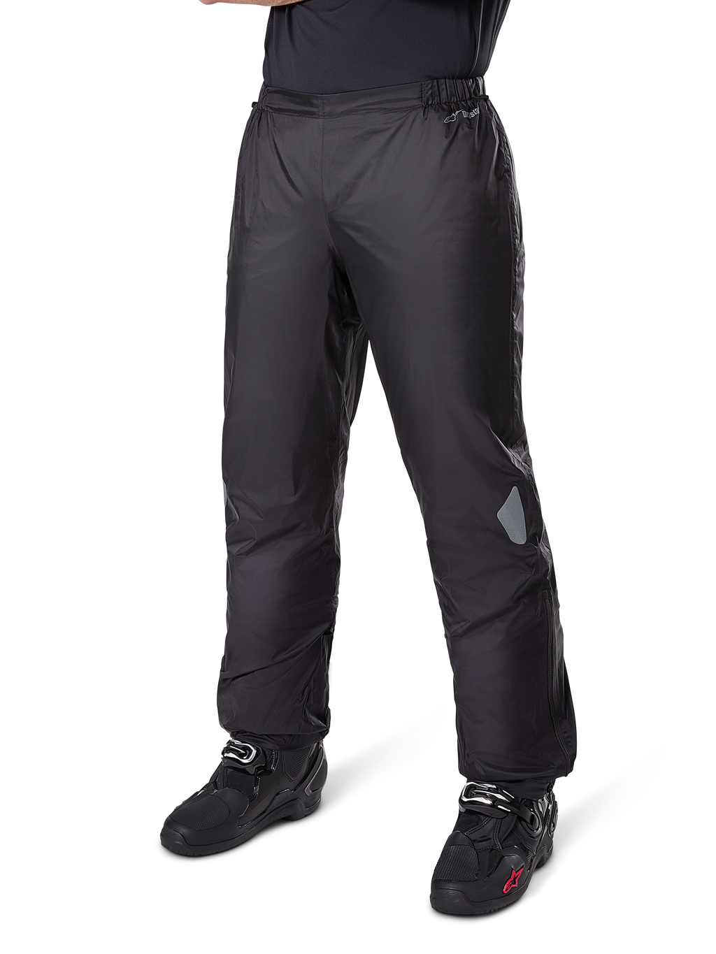 Alpinestars Bogotá Pro Drystar® 3 Seasons broek, adventure touring motorbroek, zwart, gedragen met zwarte motorlaarzen, met reflecterende patches op de knieën en Drystar-branding, lichtgewicht waterdicht textielontwerp voor rijden in alle seizoenen.