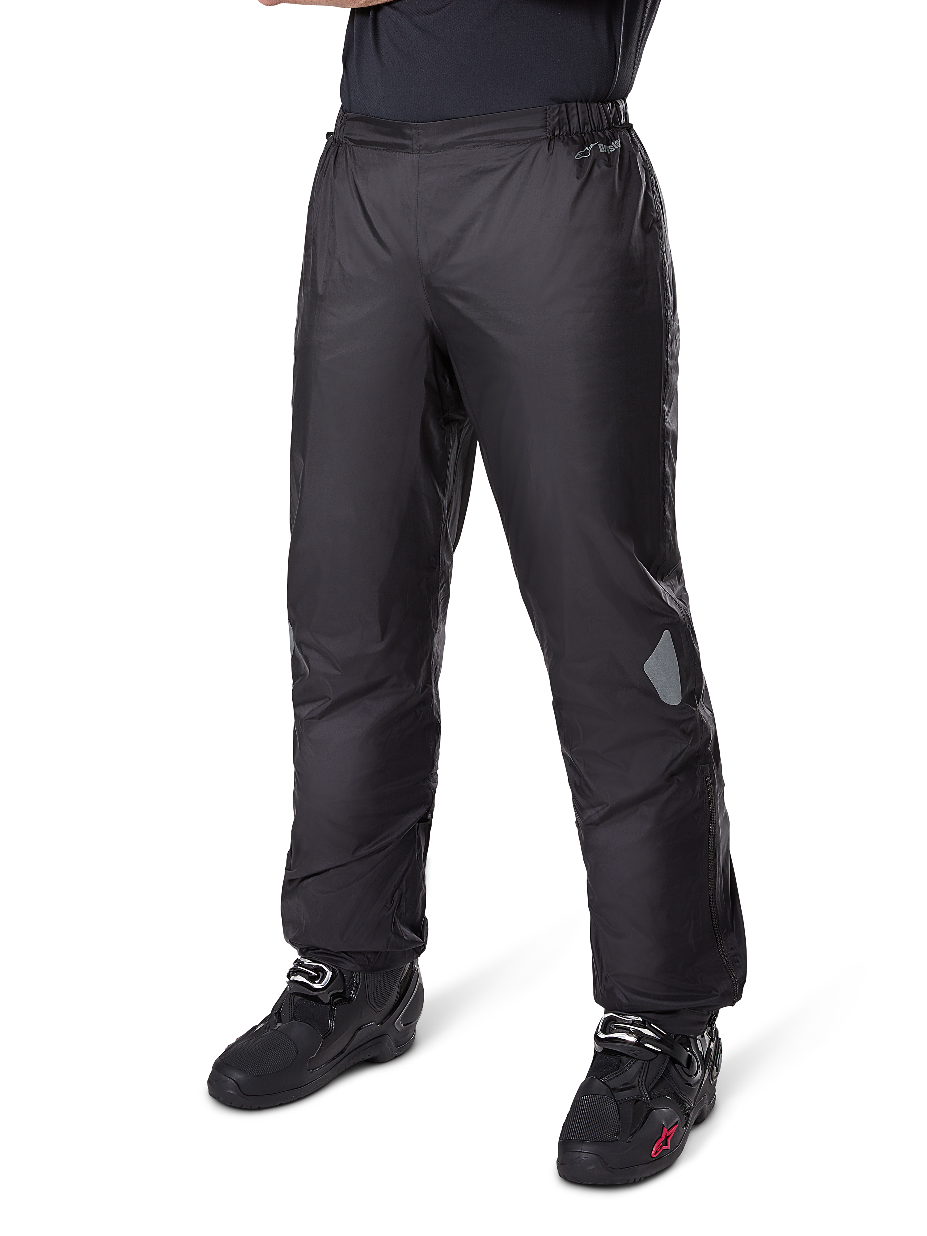 Alpinestars Bogotá Pro Drystar® 3 Seasons broek, adventure touring motorbroek, zwart, gedragen met zwarte motorlaarzen, met reflecterende patches op de knieën en Drystar-branding, lichtgewicht waterdicht textielontwerp voor rijden in alle seizoenen.