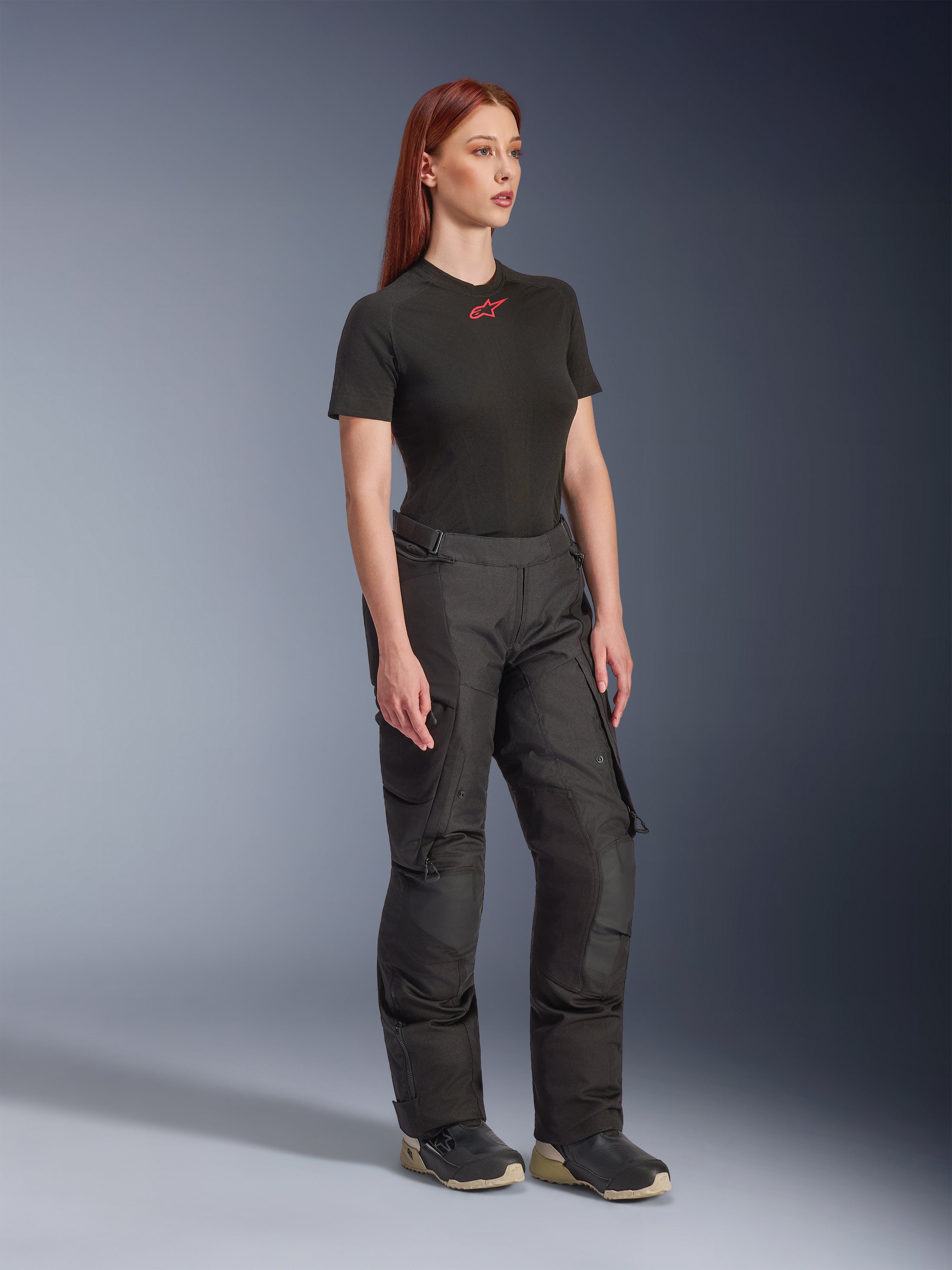 Alpinestars Stella Andes V4 Drystar® broek, motorbroek voor dames, zwart, gedragen met een zwart T-shirt met korte mouwen en rood logo en technische schoenen, adventure touring-ontwerp met versterkte panelen en ventilatieritsen, volledige lengte driekwart aanzicht