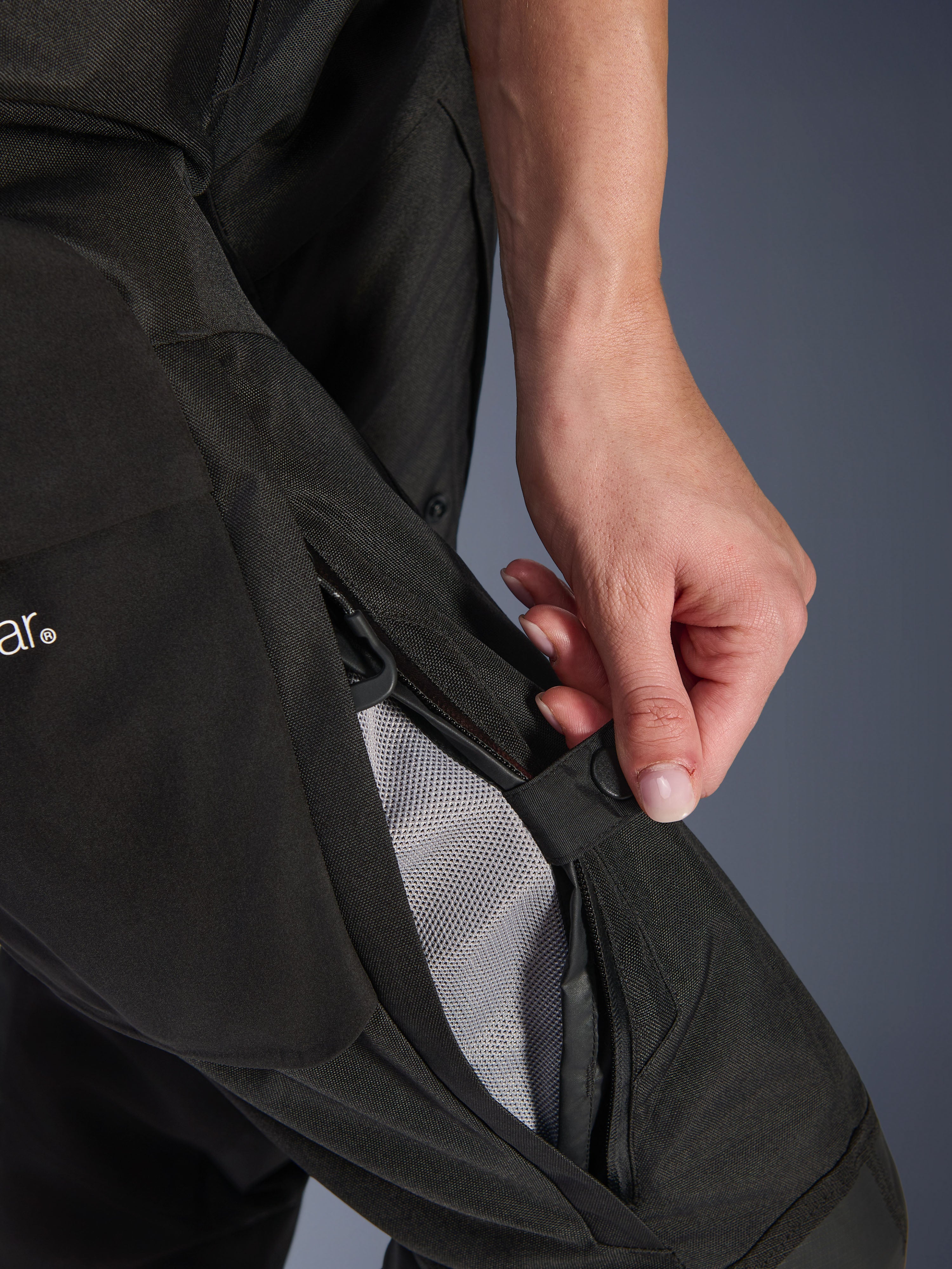 Alpinestars Stella Andes V4 Drystar® damesbroek, motorbroek, zwart, close-up van een hand die de dijventilatie met ritssluiting opent om de mesh-voering voor luchtstroom te onthullen, duurzame textiele adventure-uitrusting