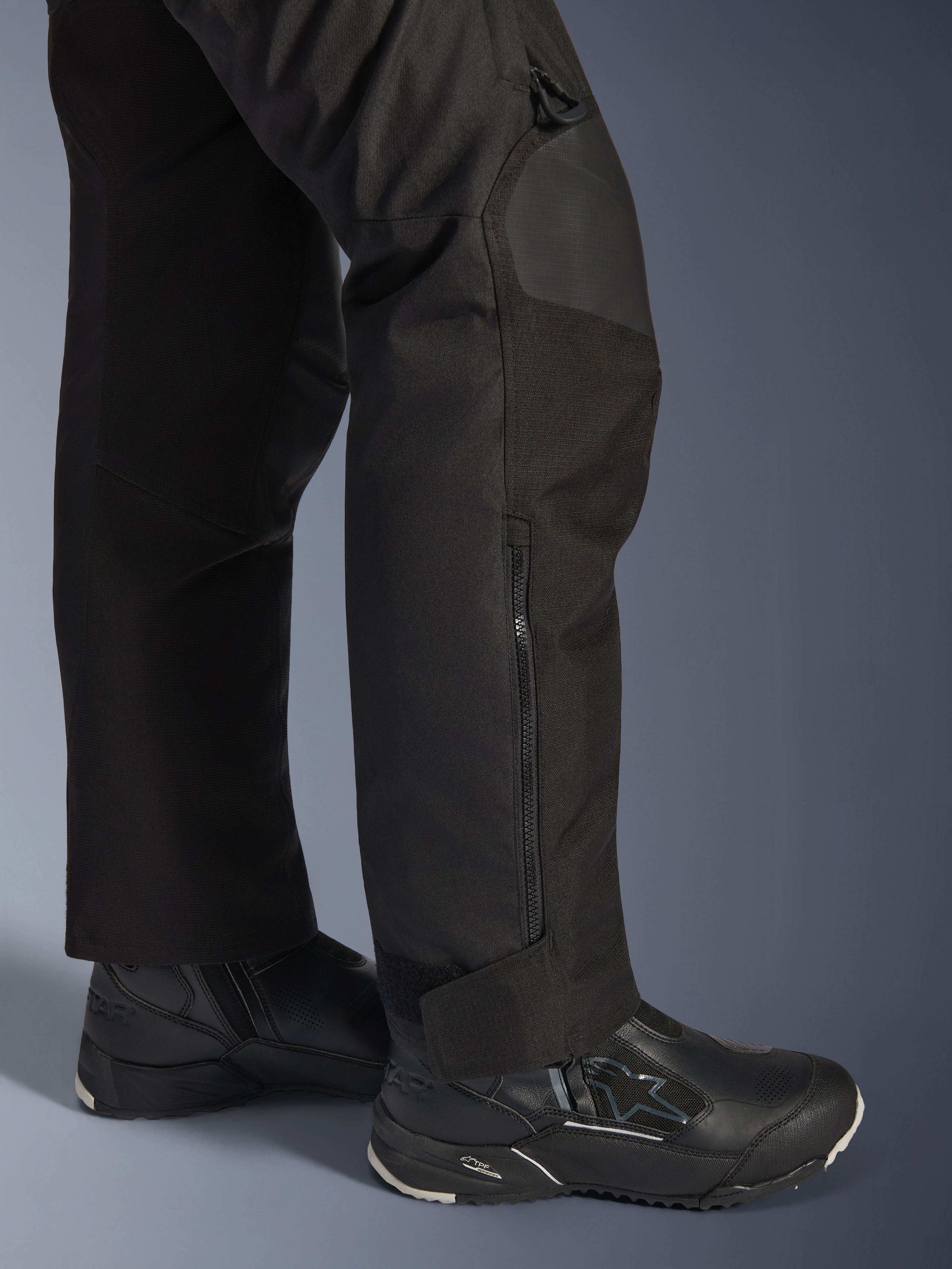 Alpinestars Stella Andes V4 Drystar® broek, motorbroek voor dames, zwart, close-up van het onderbeen met zijrits en verstelbare enkelmanchet, gedragen met zwarte Alpinestars motorlaarzen