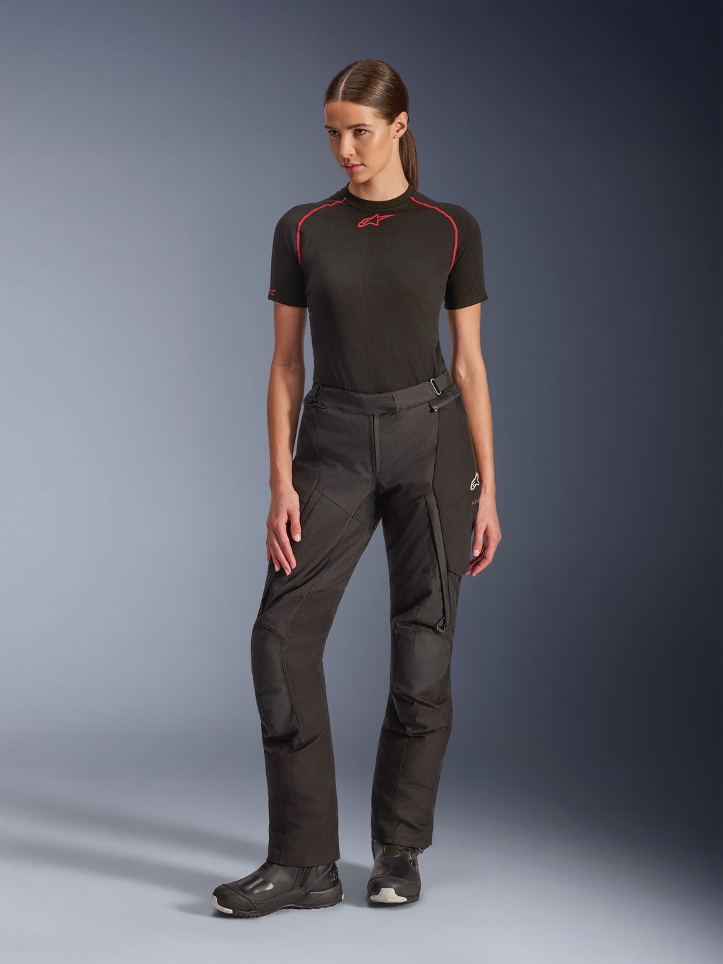 Alpinestars Stella Andes V4 Drystar® broek, adventure motorbroek voor dames, zwart, gedragen door een model met een zwarte basislaag met korte mouwen en zwarte motorlaarzen, met versterkte knieën en cargo-zakken, ergonomisch ontwerp voor toertochten in alle weersomstandigheden.