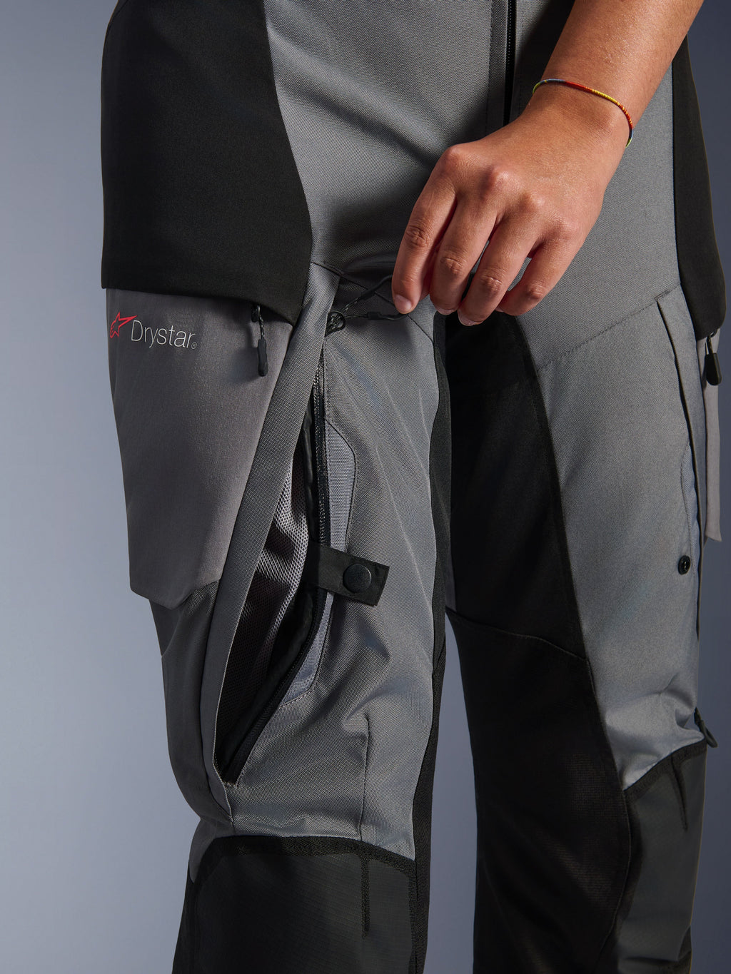 Alpinestars Stella Andes V4 Drystar Broek, zwart en donkergrijs textiel, close-up van een hand die de directe ventilatierits op de dij opent, meshvoering zichtbaar, voorzien van Drystar-logo, adventure motorkleding