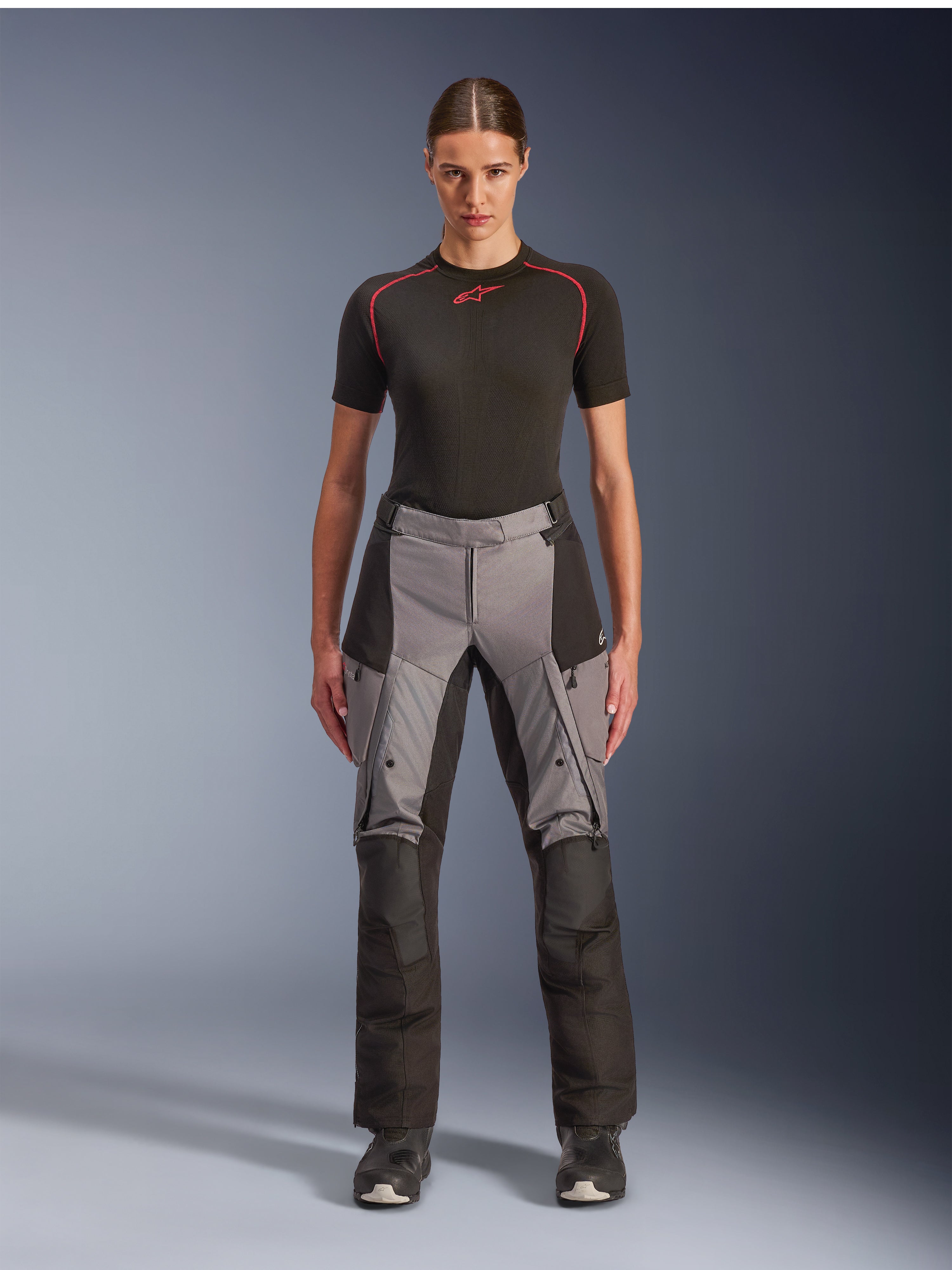 Alpinestars Stella Andes V4 Drystar broek, adventure touring motorbroek voor dames, zwart en donkergrijs, gedragen door een vrouwelijk model met een zwarte basislaag en motorlaarzen, voorzien van versterkte textielpanelen en cargozakken voor adventure ritten