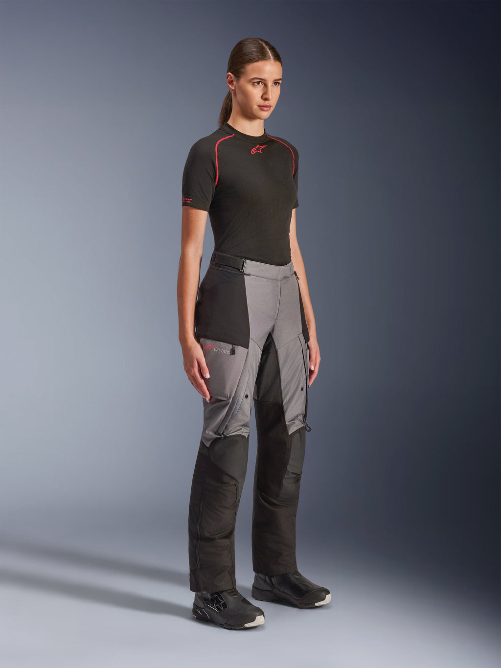 Alpinestars Stella Andes V4 Drystar® broek, adventure motorbroek voor dames, zwart en donkergrijs, gedragen door een model met een zwarte Alpinestars basislaag en zwarte laarzen, voorzien van versterkte panelen, rood Drystar-logo en cargozakken