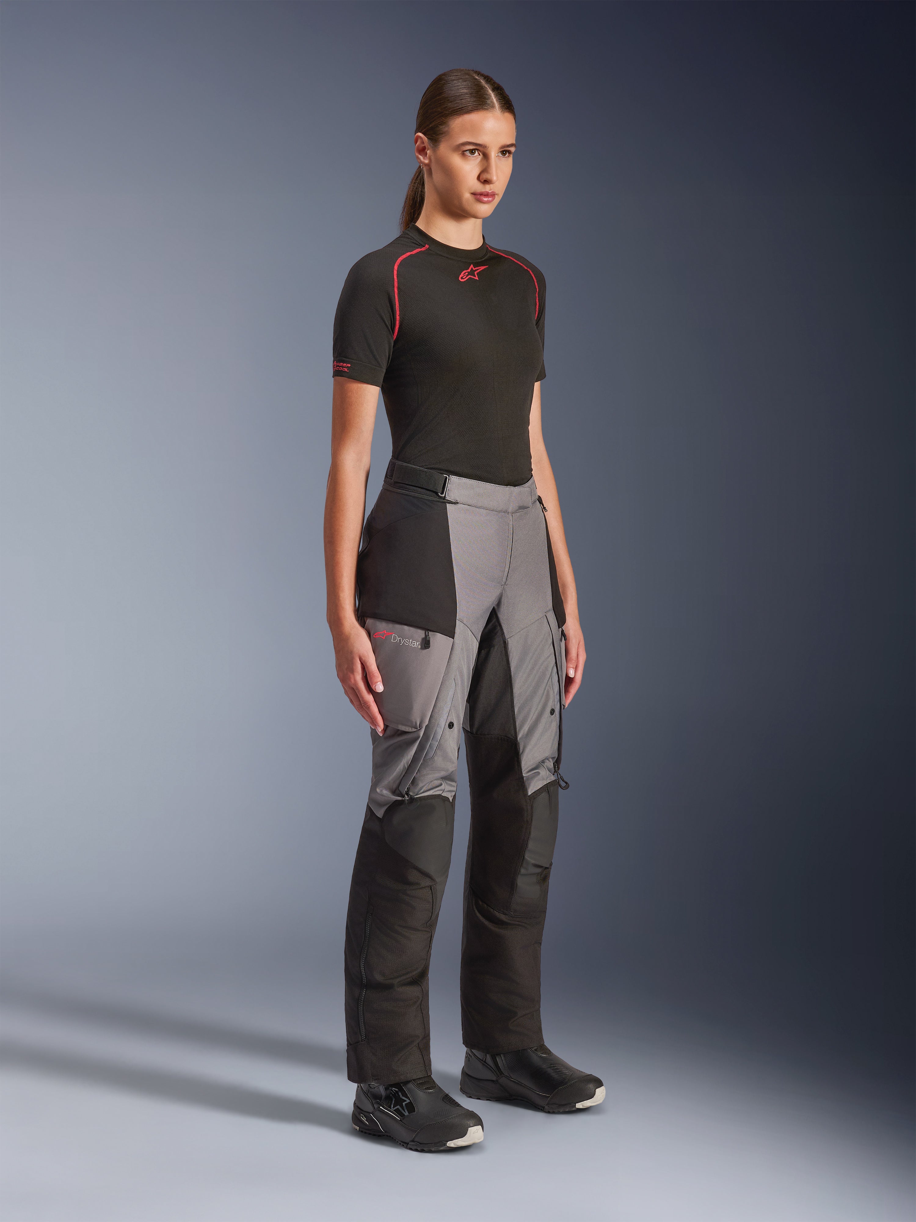 Alpinestars Stella Andes V4 Drystar® broek, adventure motorbroek voor dames, zwart en donkergrijs, gedragen door een model met een zwarte Alpinestars basislaag en zwarte laarzen, voorzien van versterkte panelen, rood Drystar-logo en cargozakken
