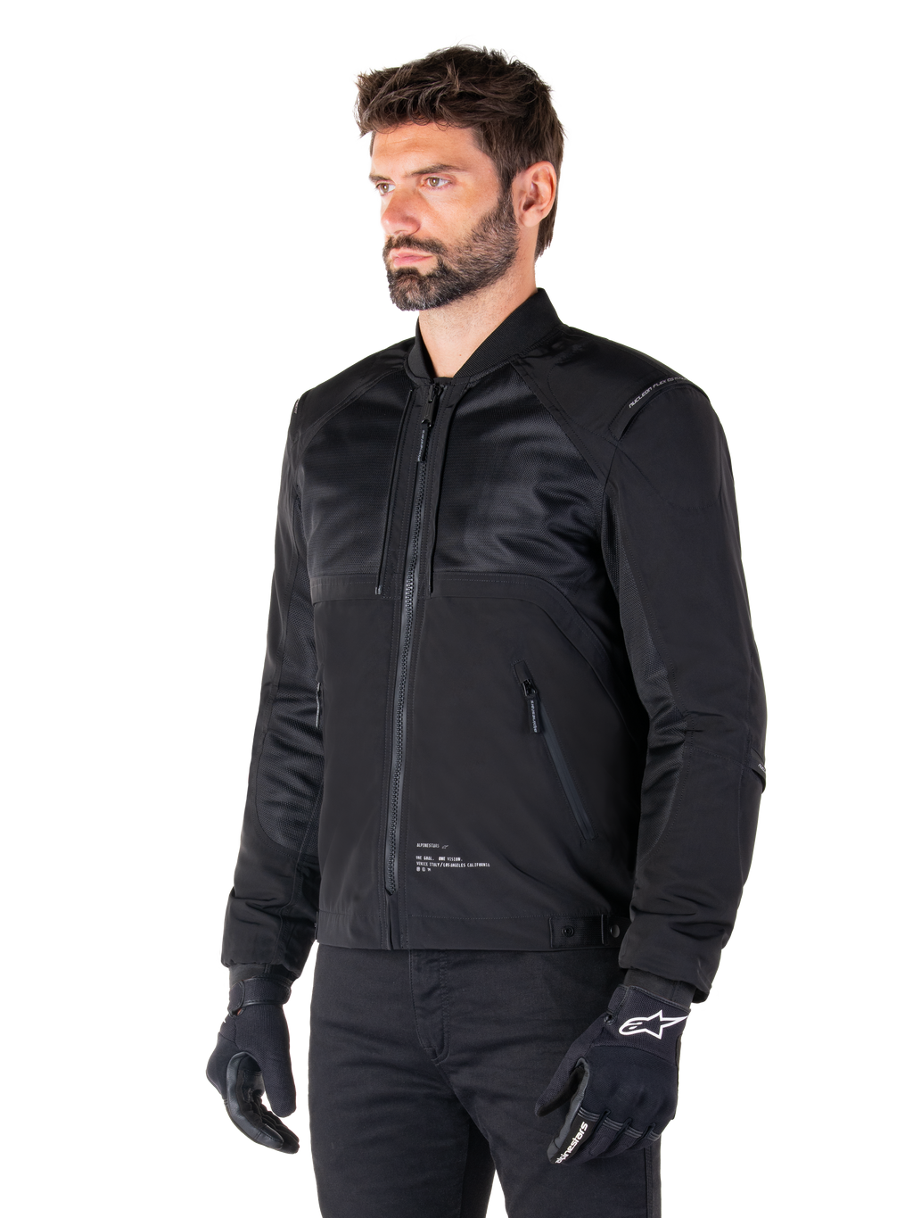 Alpinestars Mootant Waterproof Parka, modulaire zwarte motorjas getoond in de bomber-configuratie met mesh panelen op het bovenlichaam en een geribbelde kraag, gedragen door een model met zwarte motorhandschoenen en broek, urban contemporary streetwear-stijl.