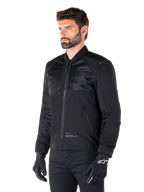 Alpinestars Mootant Waterproof Parka, modulaire zwarte motorjas getoond in de bomber-configuratie met mesh panelen op het bovenlichaam en een geribbelde kraag, gedragen door een model met zwarte motorhandschoenen en broek, urban contemporary streetwear-stijl.