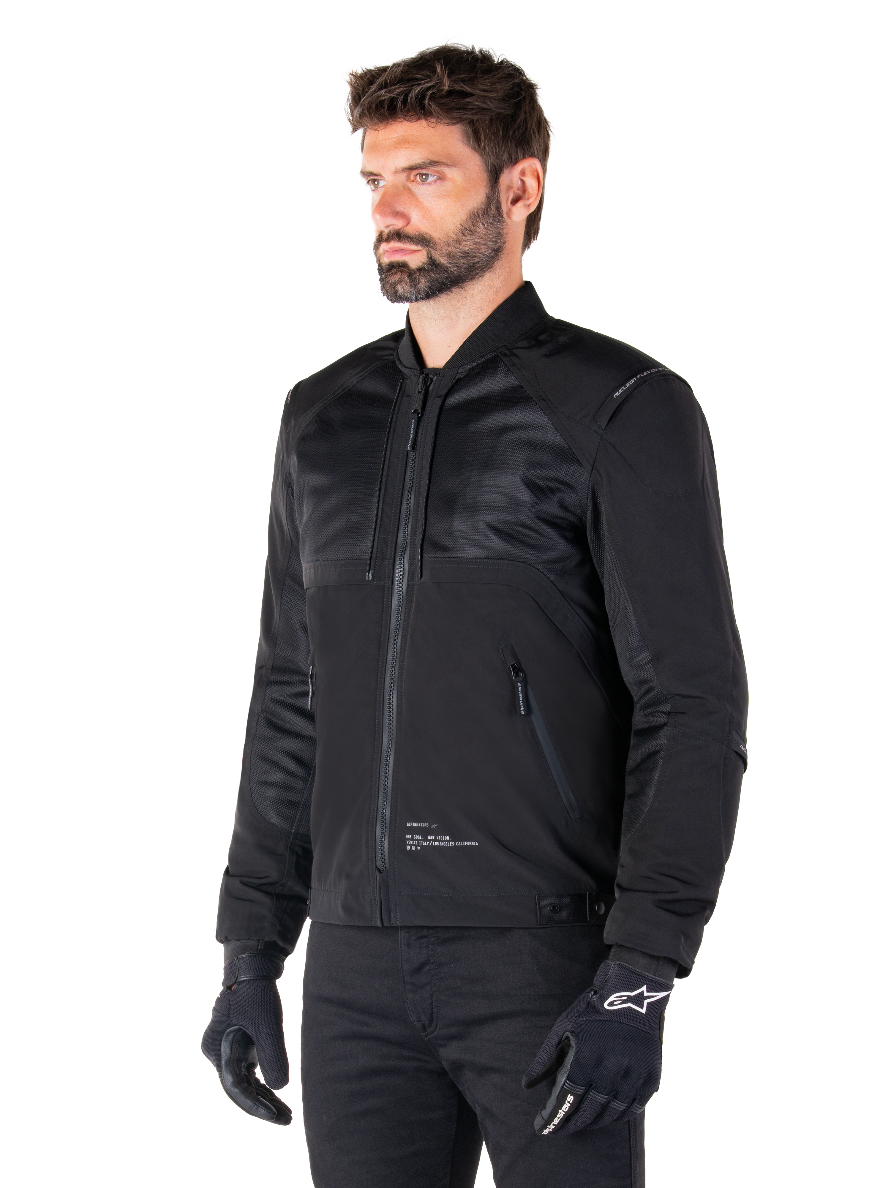 Alpinestars Mootant Waterproof Parka, modulaire zwarte motorjas getoond in de bomber-configuratie met mesh panelen op het bovenlichaam en een geribbelde kraag, gedragen door een model met zwarte motorhandschoenen en broek, urban contemporary streetwear-stijl.