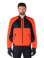 Alpinestars Mootant Waterproof Parka in Spicy Orange en zwart, modulaire motorjas getoond in een bomberjack-configuratie op een mannelijk model, met zwarte mesh panelen op de bovenborst, feloranje torso en mouwen, ritssluiting aan de voorzijde en een geribbelde kraag, gecombineerd met zwarte handschoenen en broek