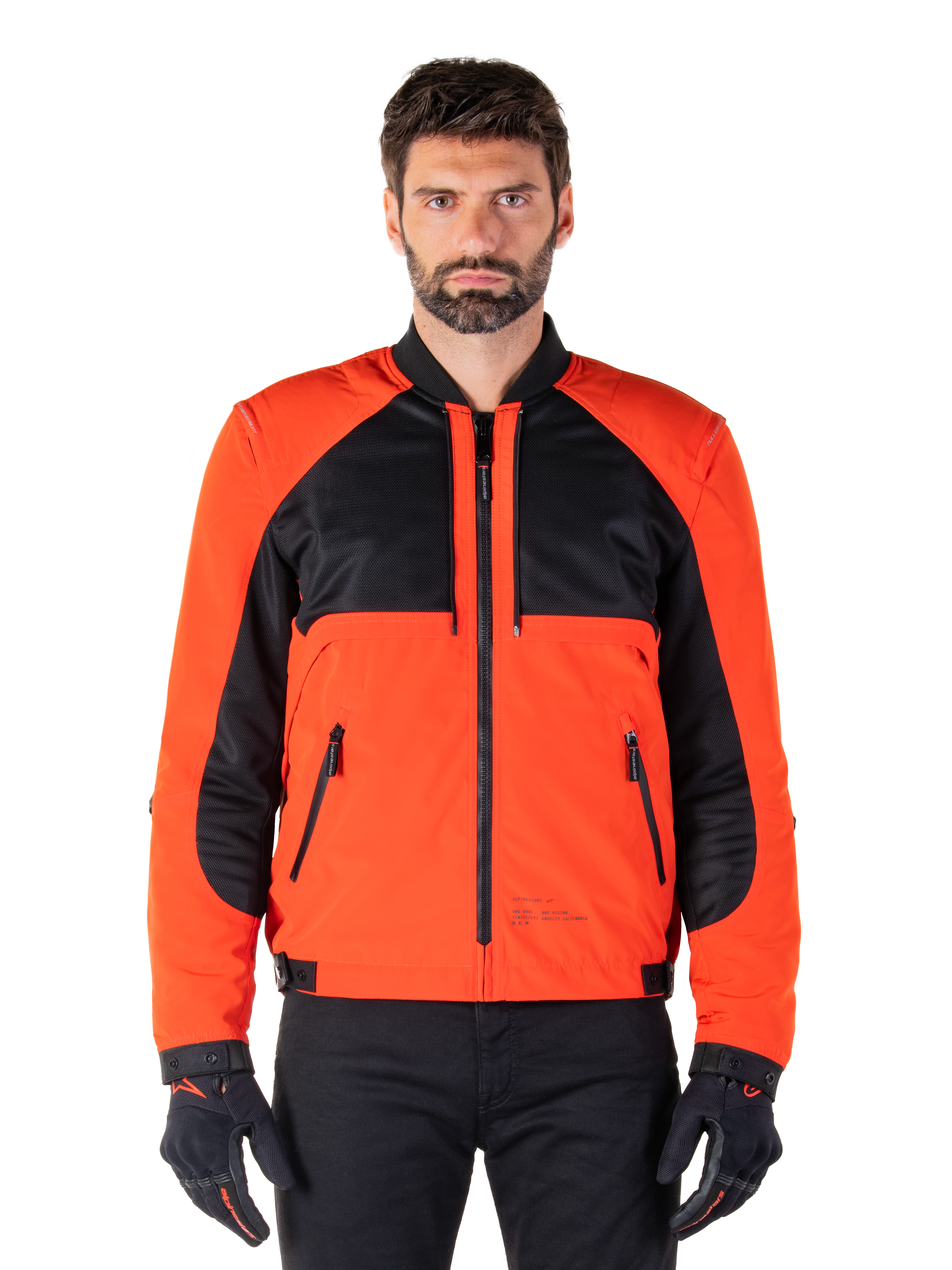 Alpinestars Mootant Waterproof Parka in Spicy Orange en zwart, modulaire motorjas getoond in een bomberjack-configuratie op een mannelijk model, met zwarte mesh panelen op de bovenborst, feloranje torso en mouwen, ritssluiting aan de voorzijde en een geribbelde kraag, gecombineerd met zwarte handschoenen en broek
