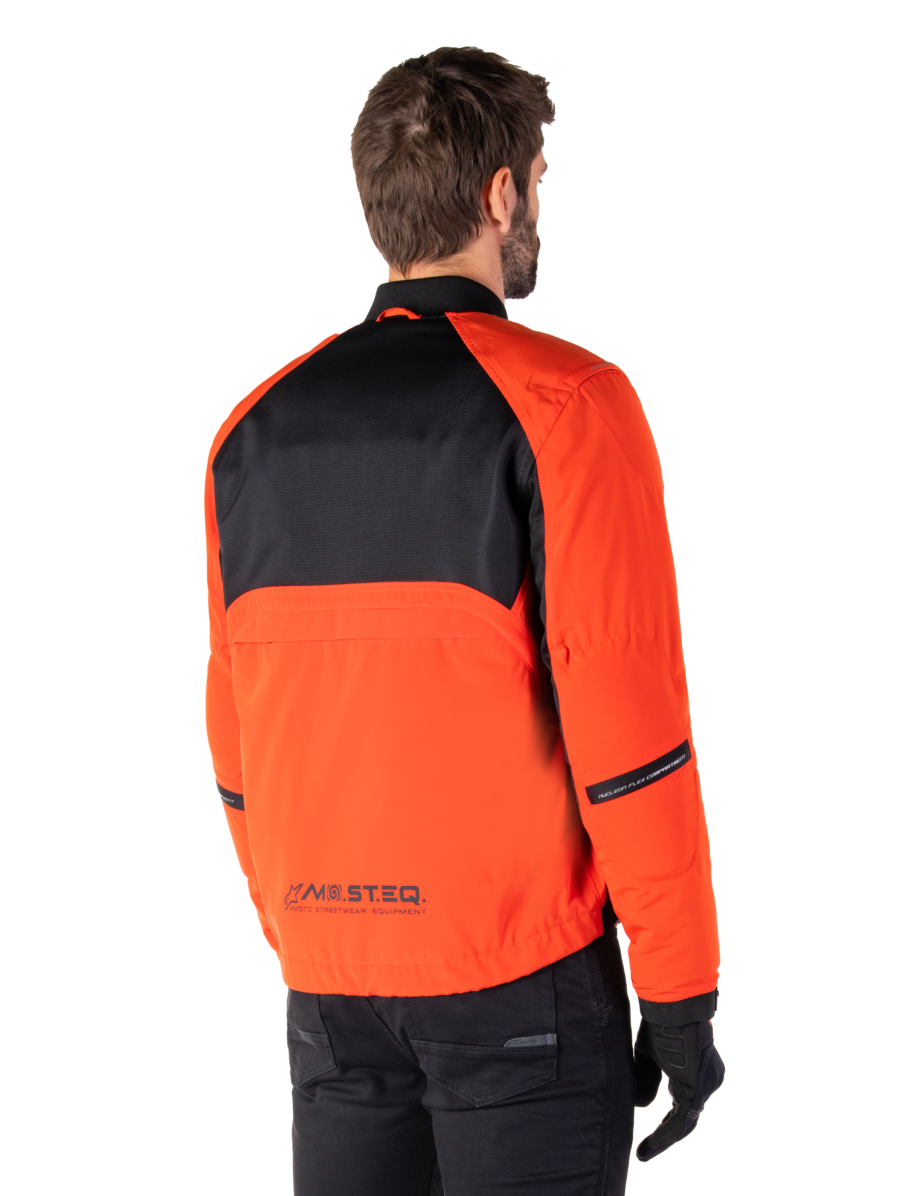 Achteraanzicht van een motorrijder die de Alpinestars Mootant Waterproof Parka draagt in Spicy Orange en zwart, voorzien van een zwart mesh paneel op de bovenrug en reflecterende MO.ST.EQ.-branding, moderne utilitaire motorjas.