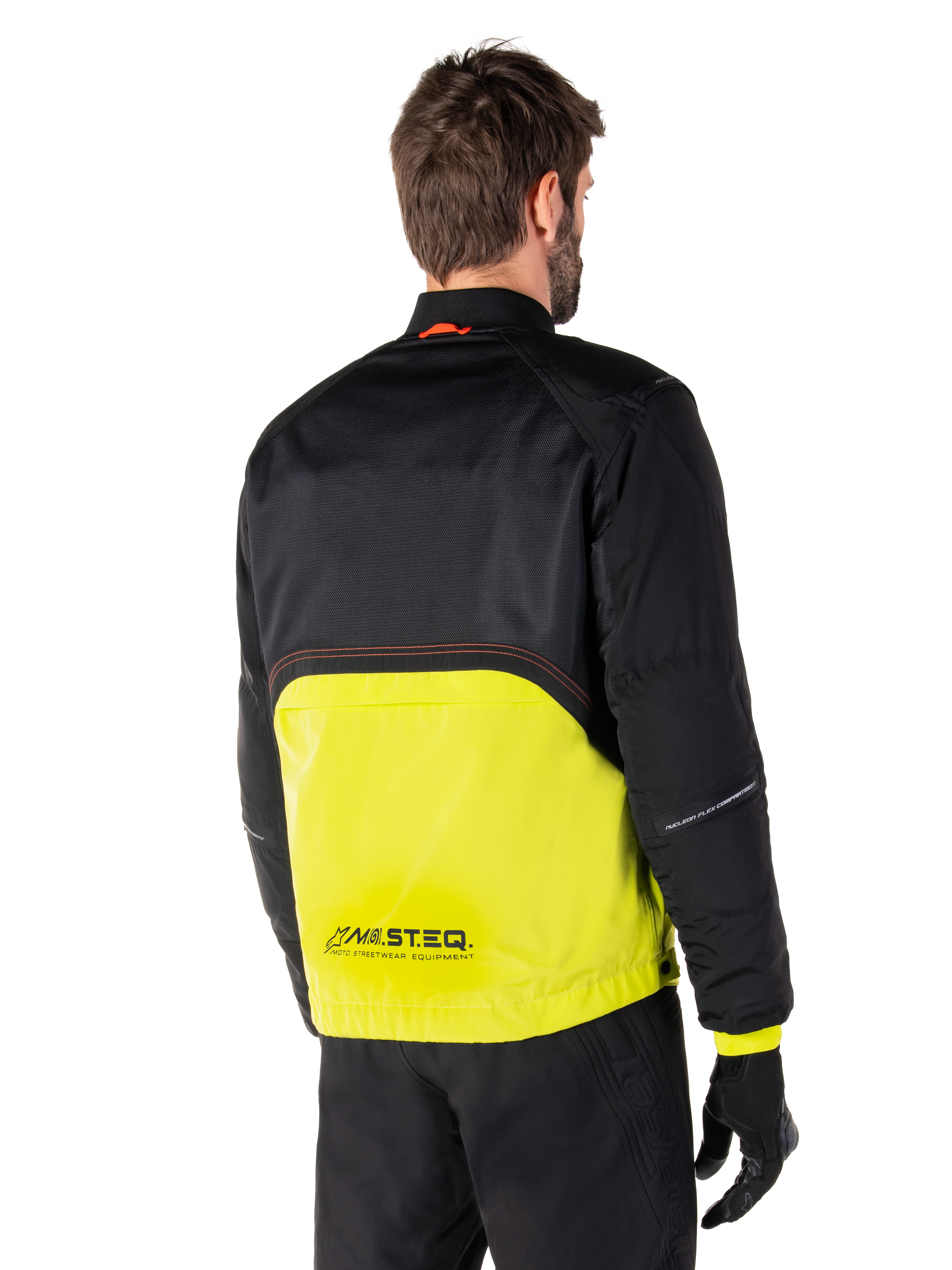 Alpinestars Mootant Waterproof Parka, motorjas, Lime Punch en zwart, achteraanzicht met zwarte mesh bovenzijde en fel limoengroen onderste deel, voorzien van MO.ST.EQ.-branding, gedragen met zwarte motorbroek en handschoenen