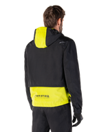 Alpinestars Mootant Waterproof Parka, achteraanzicht, Lime Punch en zwart, zwart bovendeel met een limoengeel paneel op de capuchon en de onderrug, MO.ST.EQ. branding op de zoom, gedragen met een zwarte motorbroek en handschoenen, urban contemporary motorjas