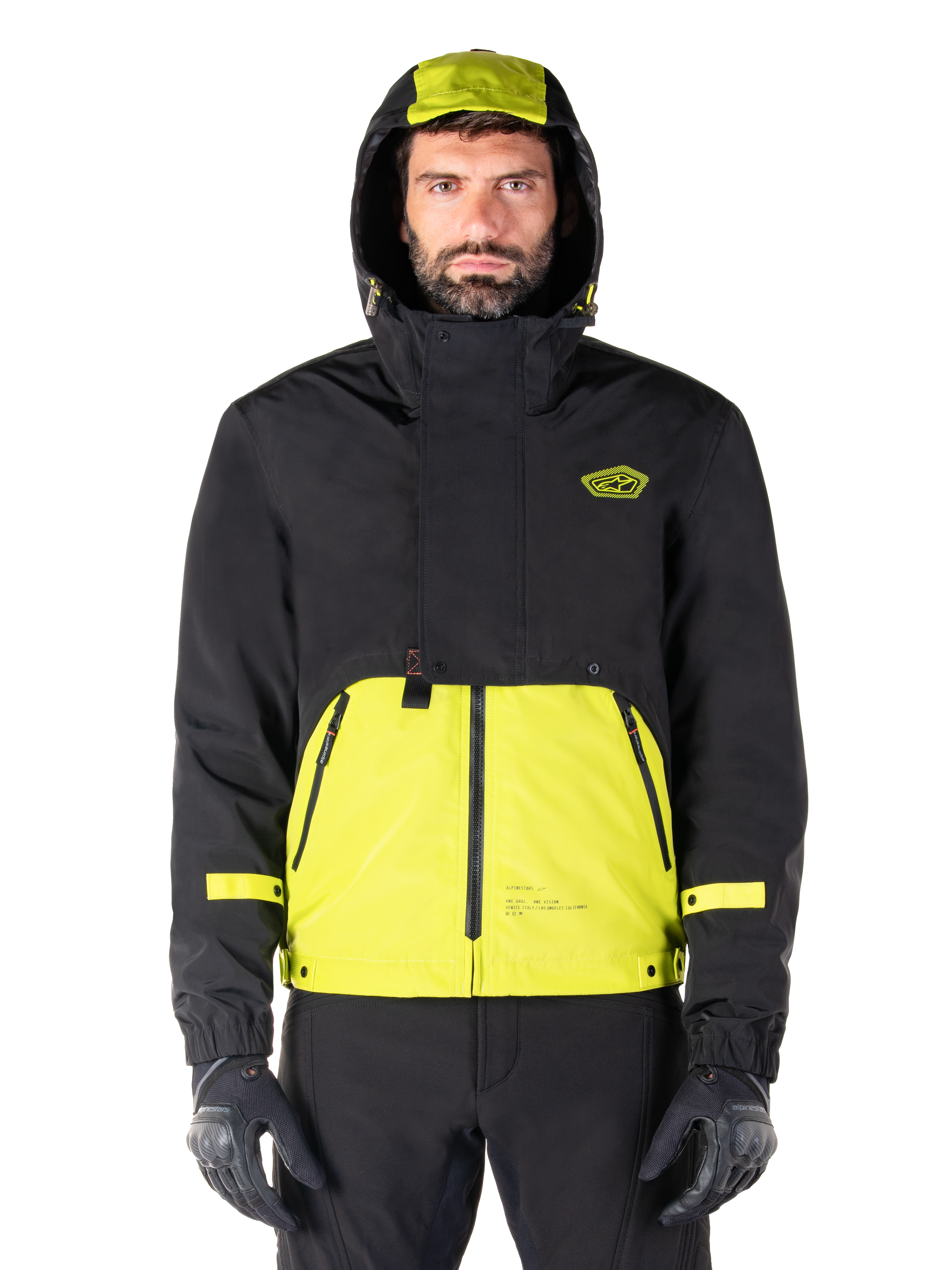 Alpinestars Mootant Waterproof Parka, Lime Punch Black motorjas, vooraanzicht, modulair 3-in-1 ontwerp met zwart bovengedeelte en fel limoengroen ondergedeelte, voorzien van een capuchon met trekkoord en logo op de borst, gedragen met zwarte broek en motorhandschoenen