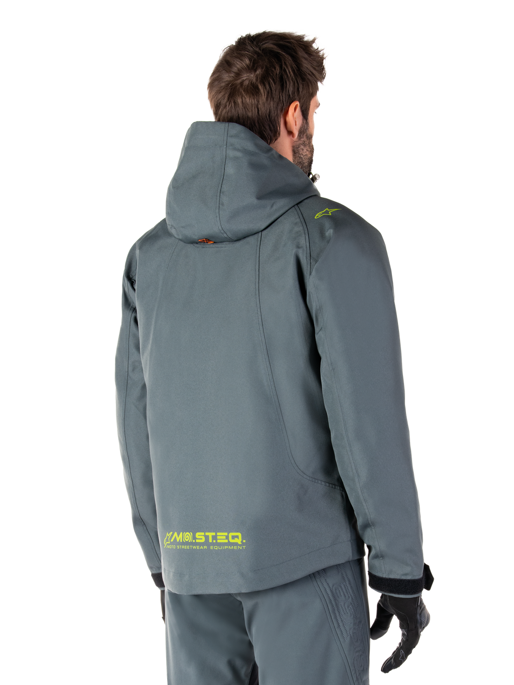 Alpinestars Morush Waterproof Parka in Urban Gray, achteraanzicht, met gele MO.ST.EQ. branding op de onderrug en schouder, minimalistisch ontwerp met capuchon, gedragen met bijpassende grijze motorbroek en zwarte handschoenen, urban motor-streetwear.