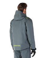 Alpinestars Morush Waterproof Parka in Urban Gray, achteraanzicht, met gele MO.ST.EQ. branding op de onderrug en schouder, minimalistisch ontwerp met capuchon, gedragen met bijpassende grijze motorbroek en zwarte handschoenen, urban motor-streetwear.