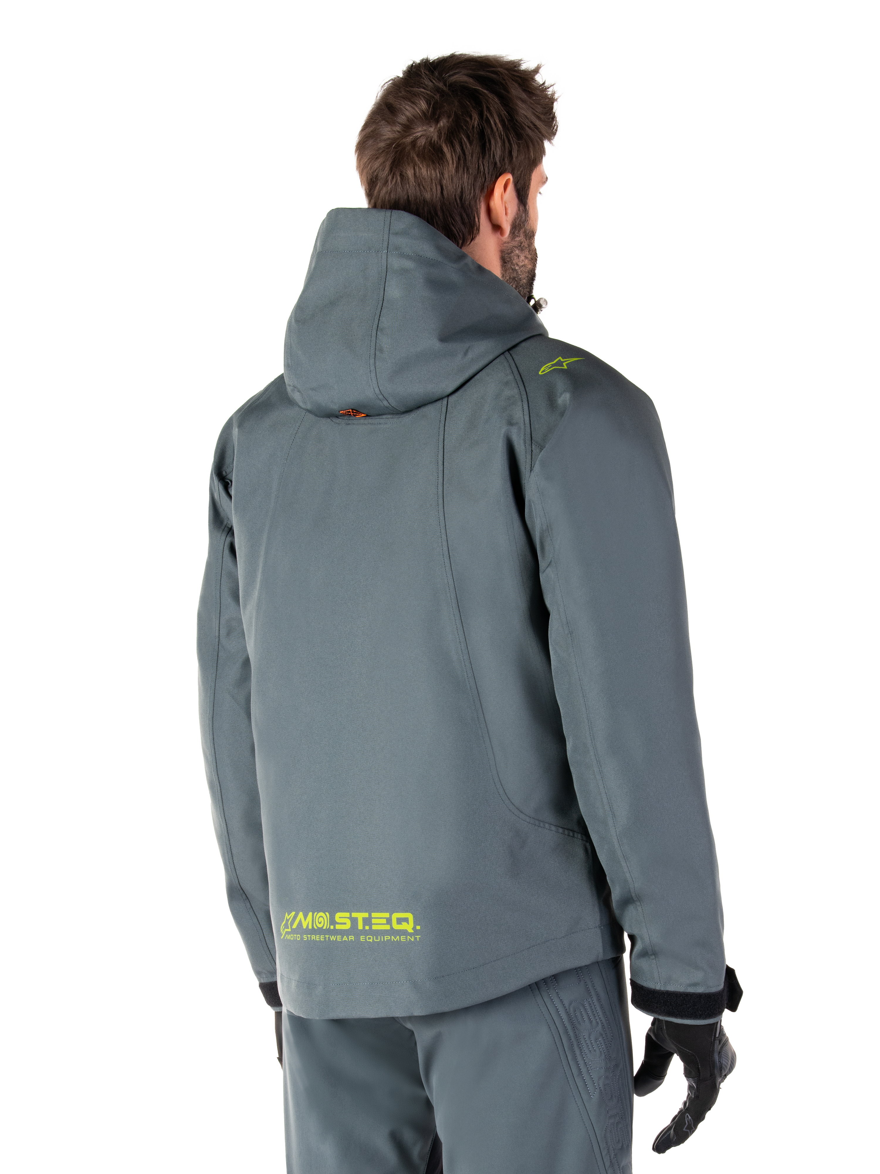 Alpinestars Morush Waterproof Parka in Urban Gray, achteraanzicht, met gele MO.ST.EQ. branding op de onderrug en schouder, minimalistisch ontwerp met capuchon, gedragen met bijpassende grijze motorbroek en zwarte handschoenen, urban motor-streetwear.