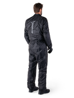 Alpinestars Hurricane Rain V2-pak, zwart eendelig waterdicht motorregenpak, achteraanzicht met groot verticaal reflecterend logo, lichtgewicht windbestendige stof, gedragen met zwarte handschoenen en laarzen