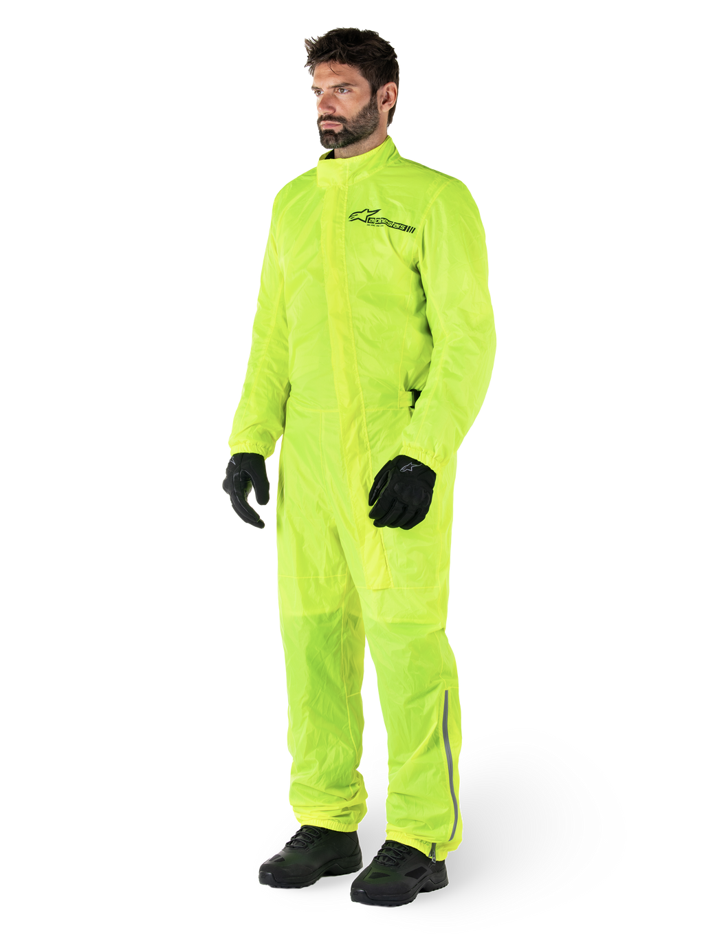 Alpinestars Hurricane Rain V2 Pak, eendelig waterdicht motorregenpak, fluoriserend geel, gedragen met zwarte handschoenen en laarzen, voorzien van een zwart Alpinestars-logo op de borst en reflecterende details op de benen