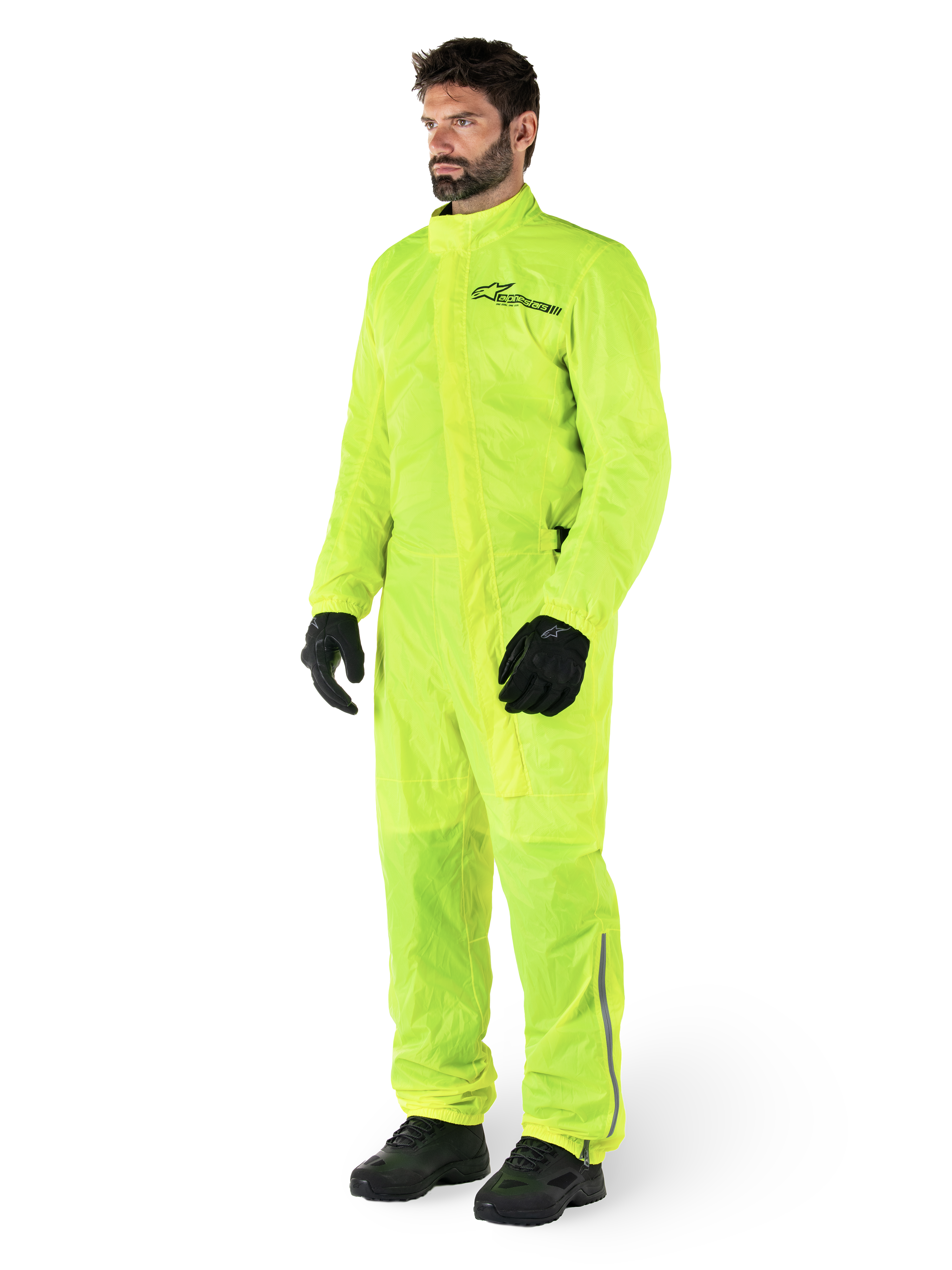 Alpinestars Hurricane Rain V2 Pak, eendelig waterdicht motorregenpak, fluoriserend geel, gedragen met zwarte handschoenen en laarzen, voorzien van een zwart Alpinestars-logo op de borst en reflecterende details op de benen