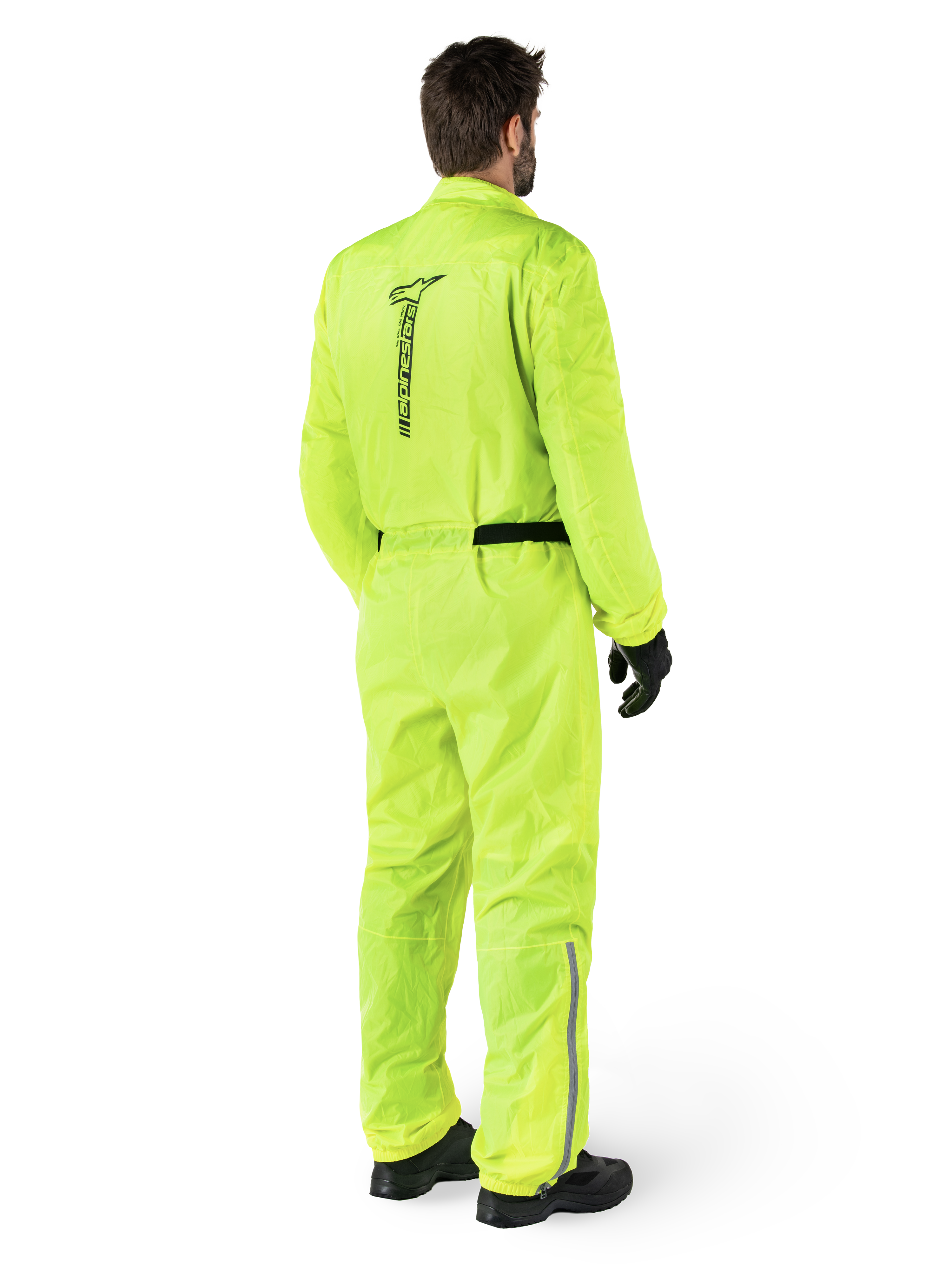 Alpinestars Hurricane Rain V2-pak, Yellow Fluo, achteraanzicht van een rijder die een eendelig motorregenpak draagt, met een zwart Alpinestars-logo op de rug, een zwarte tailleband en reflecterende strips op de onderbenen, gedragen met zwarte handschoenen en laarzen