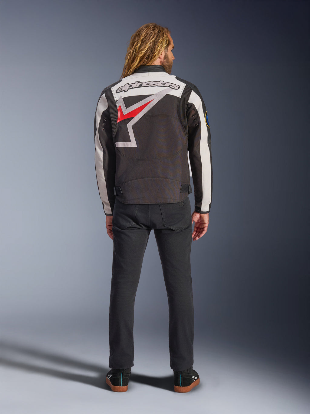 Alpinestars Axton Jacket, motorjas, zwart, off-white en felrood, achteraanzicht op een model, met een groot Alpinestars sterlogo op de rug, off-white mouwpanelen, gedragen met een zwarte broek, vintage-geïnspireerd racing teamwear ontwerp