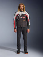 Alpinestars Axton Jacket, motorjas, zwart, gebroken wit en felrood, gedragen door een model met een zwarte broek en sneakers, voorzien van een opvallend rondom lopend logo en een vintage op de racerij geïnspireerd ontwerp