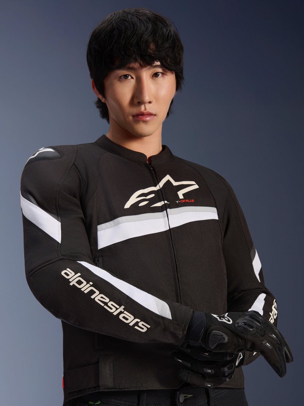 Alpinestars T-GP Plus R V4 Jacket, Black and White, worn by a male model, textile motorcycle jacket with white stripes across the chest and sleeves, Alpinestars logo on the chest, paired with black riding gloves